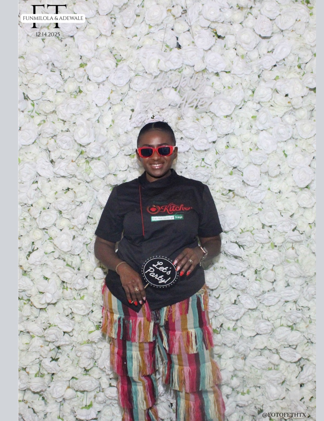 Child wearing red sunglasses, black shirt, colorful striped pants, standing in front of a white floral background.