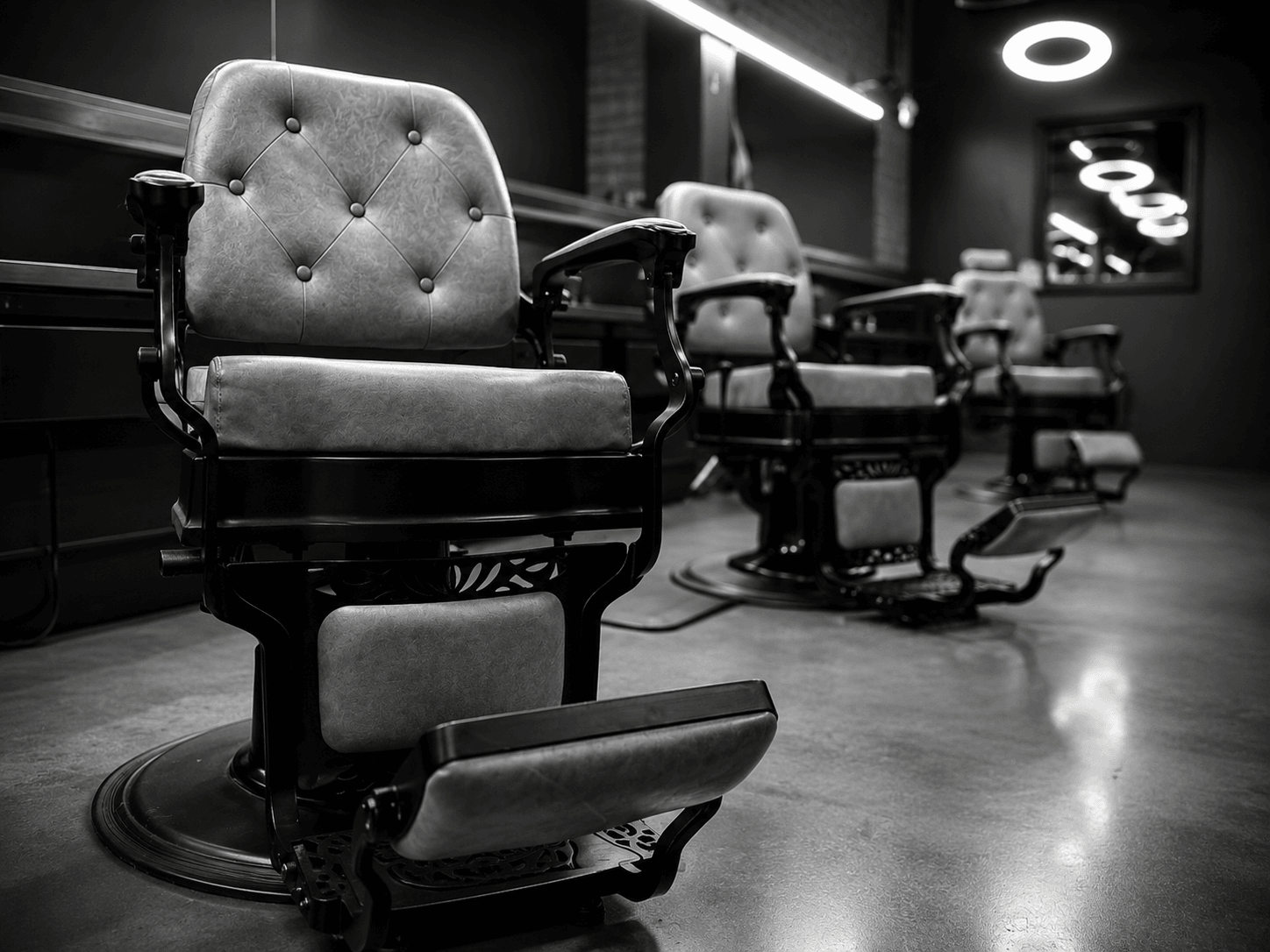 Three vintage barber chairs in a dimly lit salon, with illuminated signs on the wall, black and white photo, 20 words