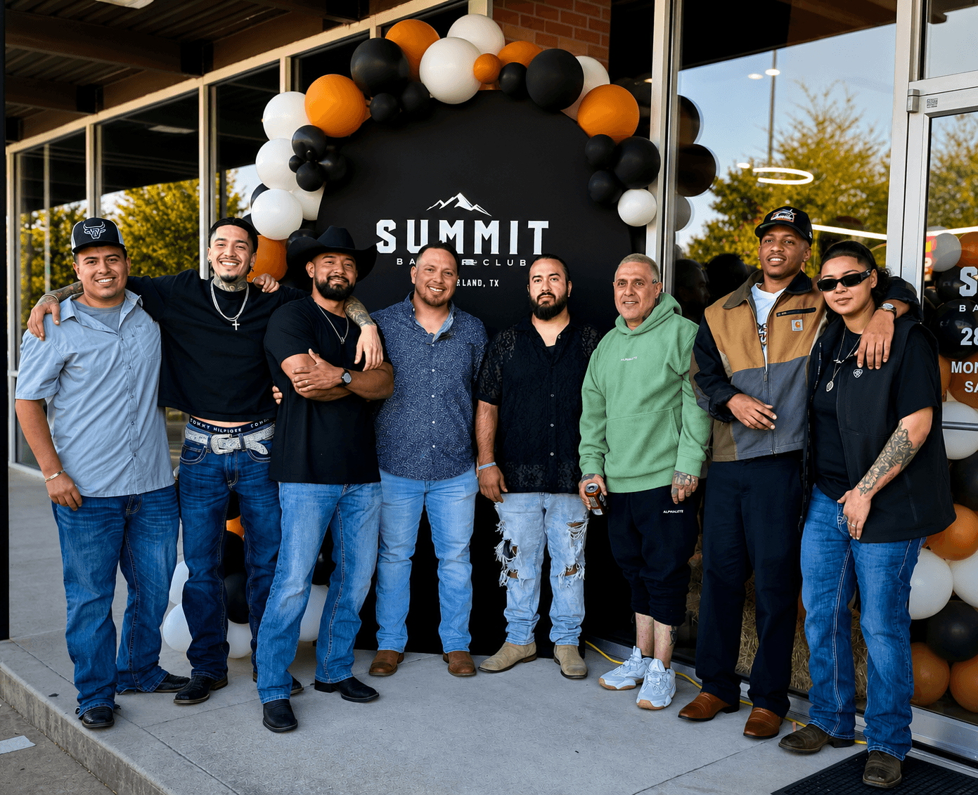 Group of nine people standing outside in front of a black and white balloon arch and a sign that says 'SUMMIT'.