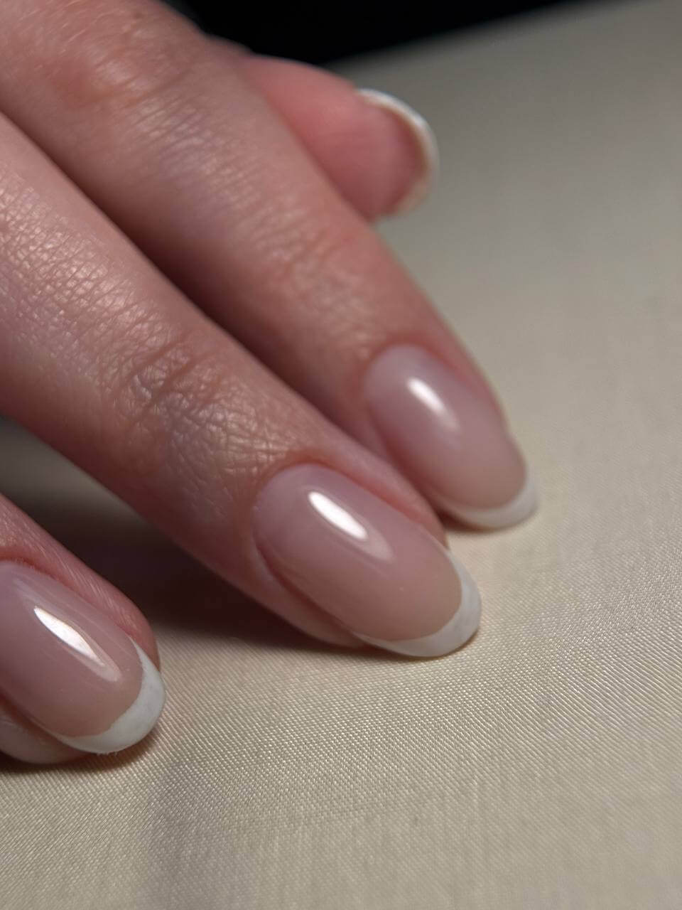 Close-up of three fingers with well-manicured nails, showing natural pink color and white tips, resting on a light surface.