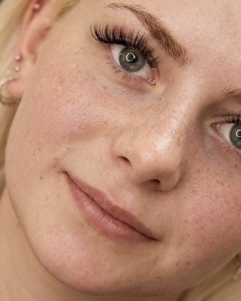 Close-up of a woman's face showing her eye, cheek, and part of her lips with freckles and makeup.