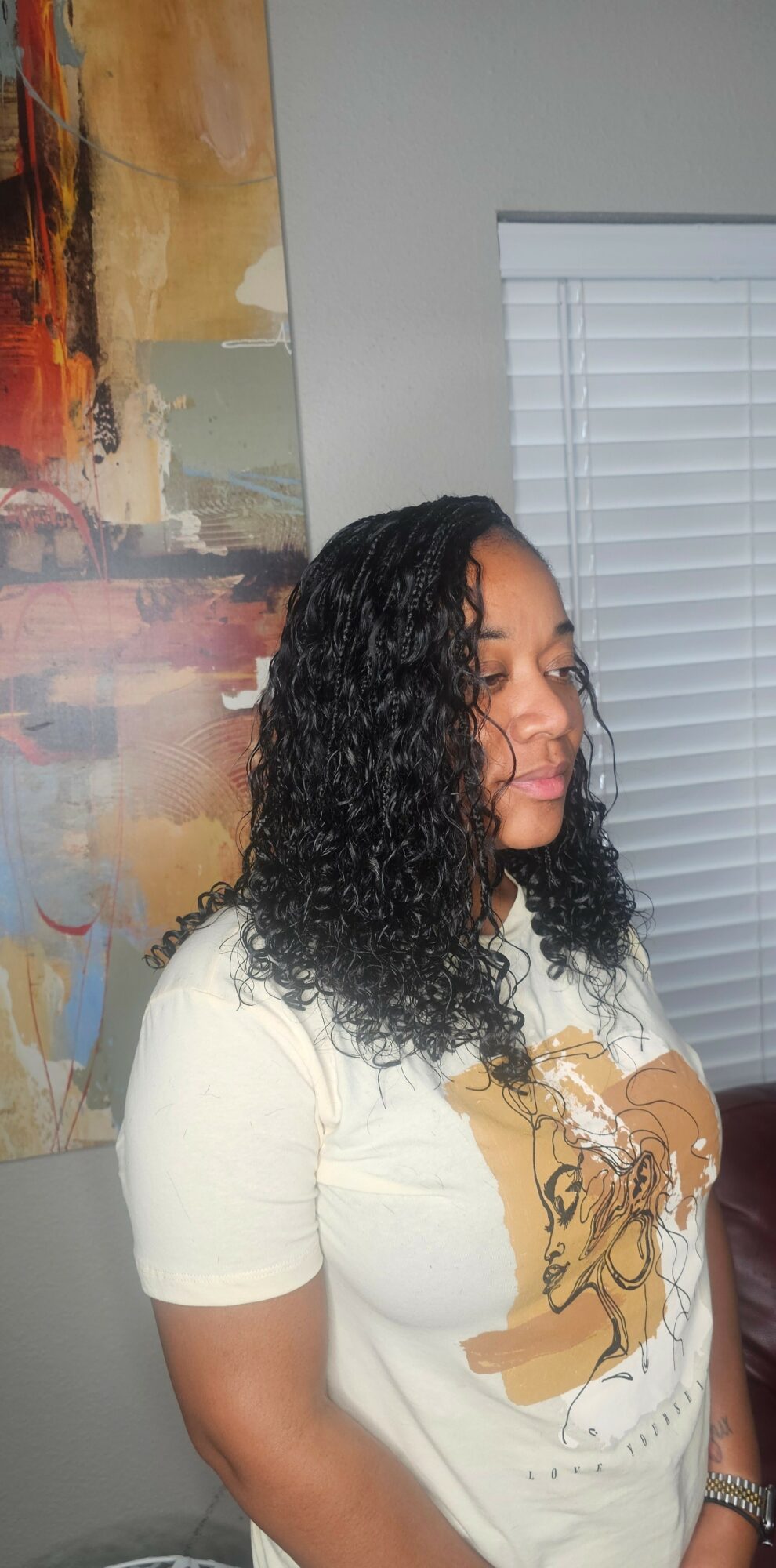 Woman with curly hair wearing a white shirt, standing indoors near a window and colorful artwork.