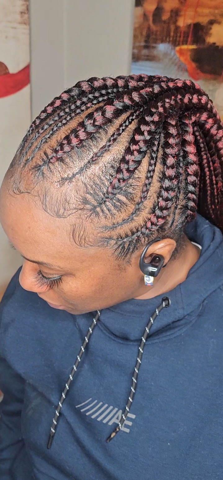 Side view of a person with braided hairstyle, wearing a navy hoodie and wireless earbud, indoors.