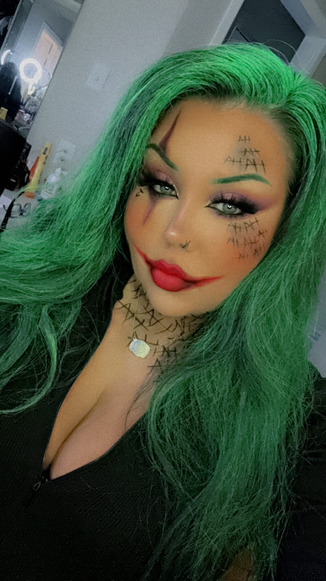Woman with bright green hair, makeup, tattoos, and jewelry, smiling slightly, indoors.
