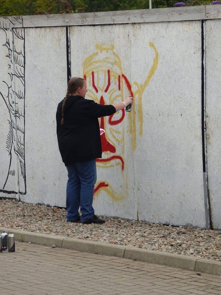 Person with dark clothing and long hair painting graffiti on a concrete wall, with a colorful design. Word count: 20.