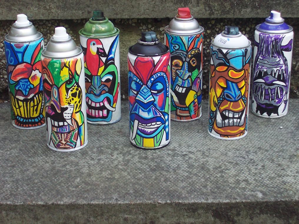 Eight colorful spray paint cans with various abstract and face-like designs, arranged on a concrete surface.