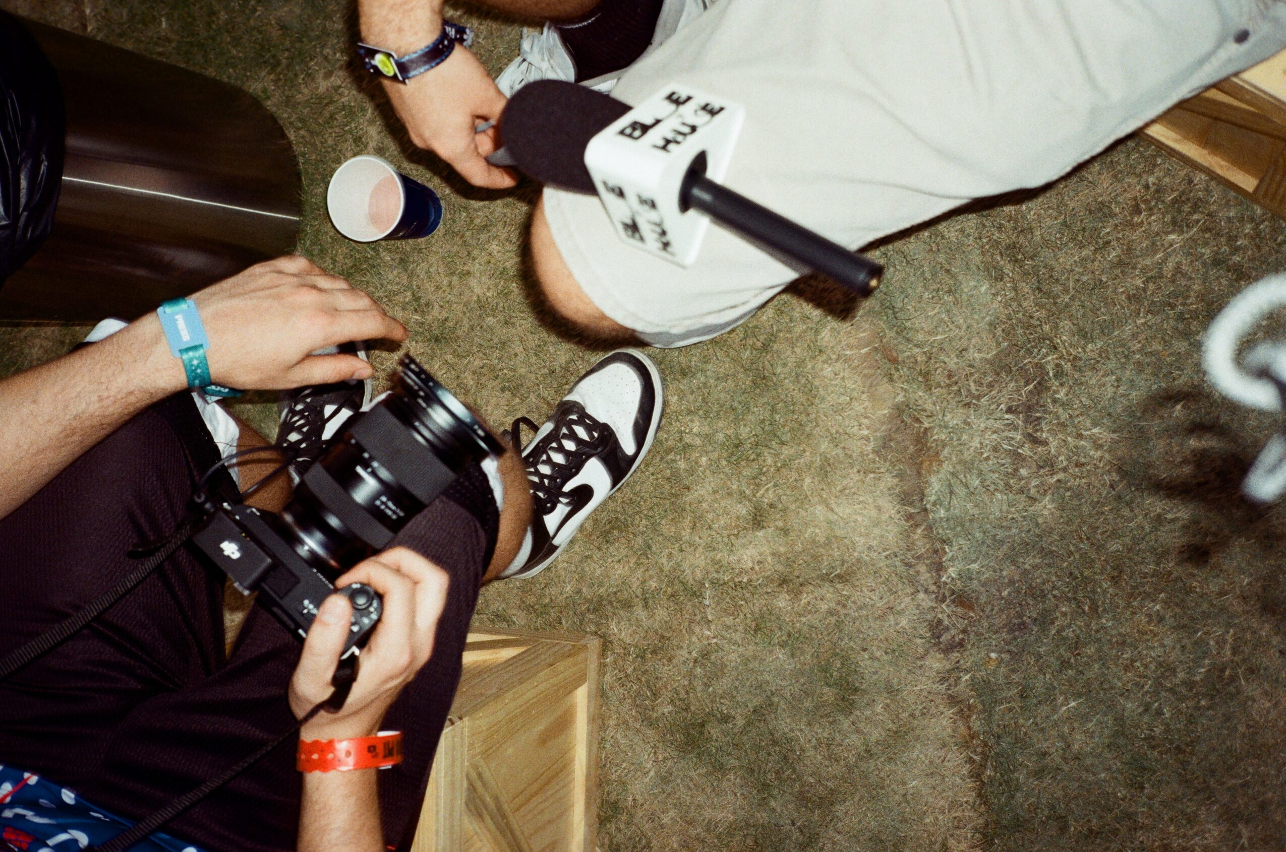 People sitting on a carpeted floor, one holding a camera, with shoes and a cup nearby.