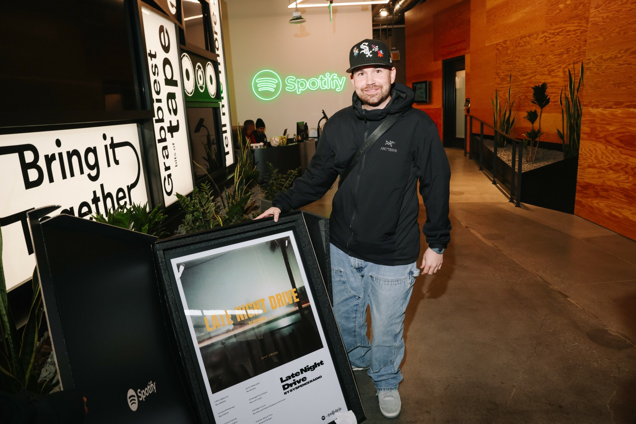 Man standing next to a digital kiosk in a modern indoor space with plants and signs, smiling at the camera.