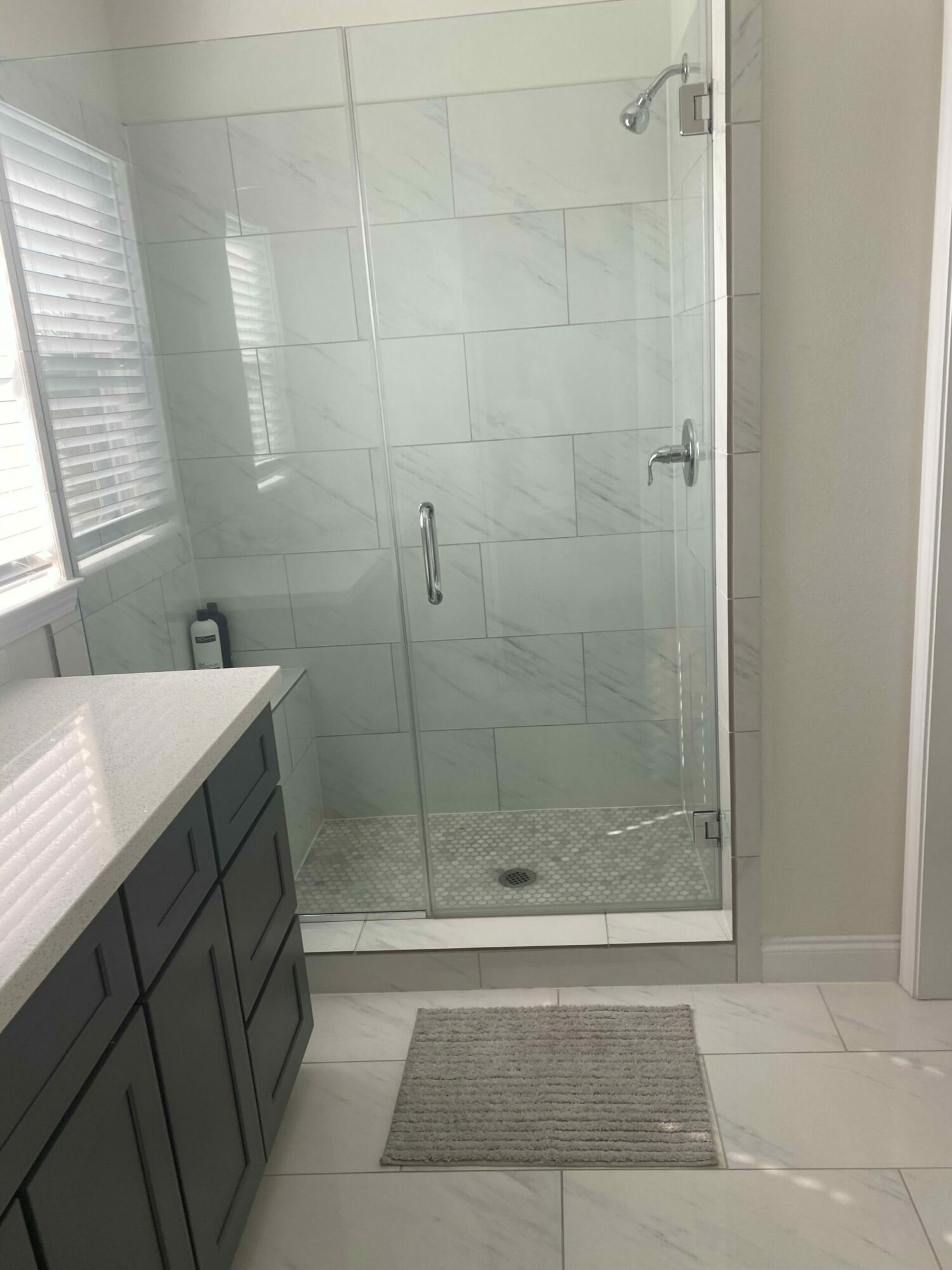 Shower area with glass door, tiled walls, and a drain, viewed from outside the shower.