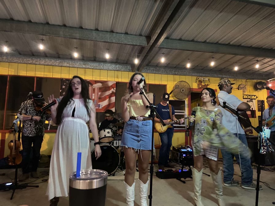 Group of people performing music on stage with microphones and instruments in a decorated indoor venue.