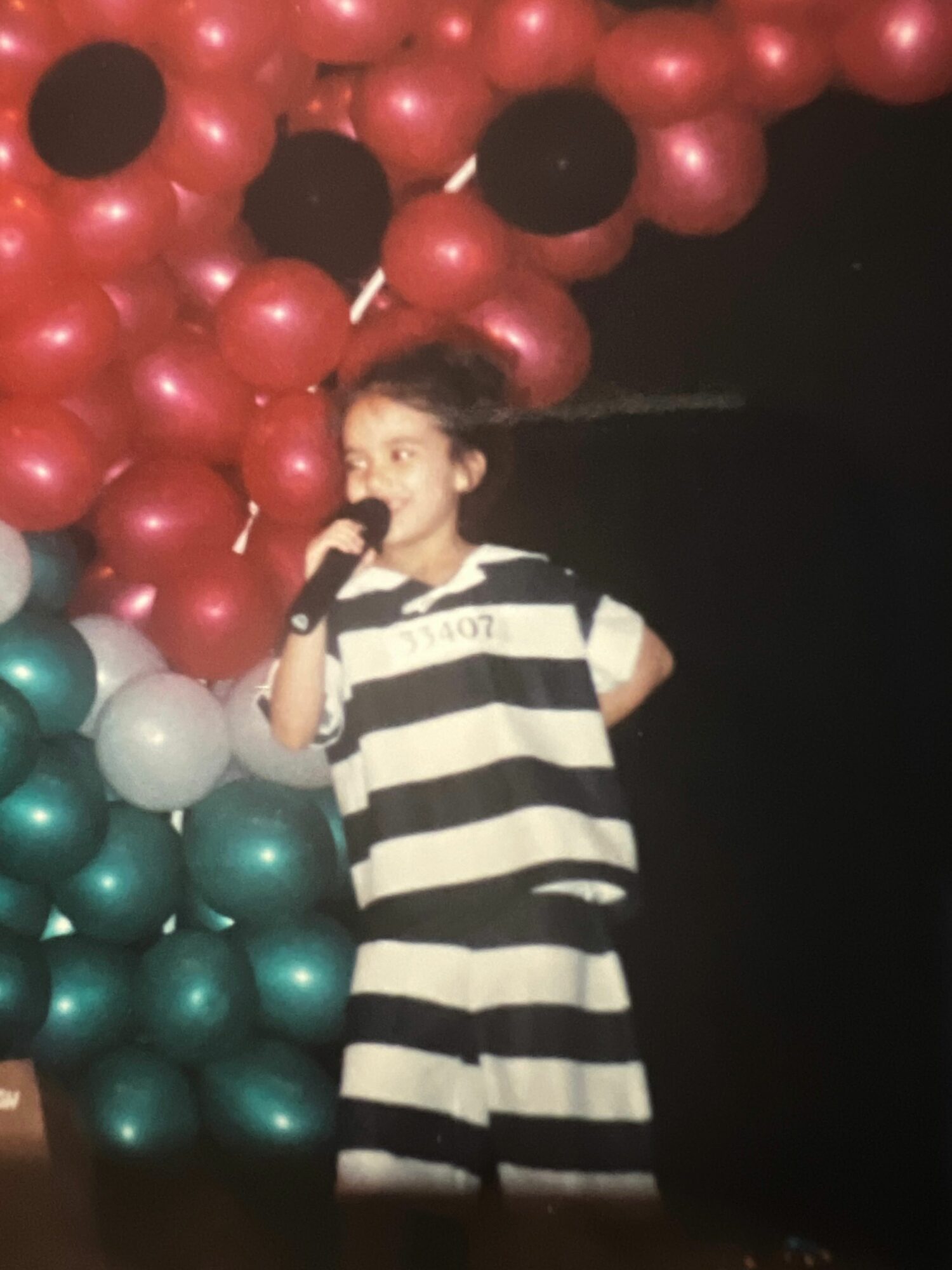 Person lying among red, white, and teal balloons, wearing a black and white striped shirt, in a dark setting.