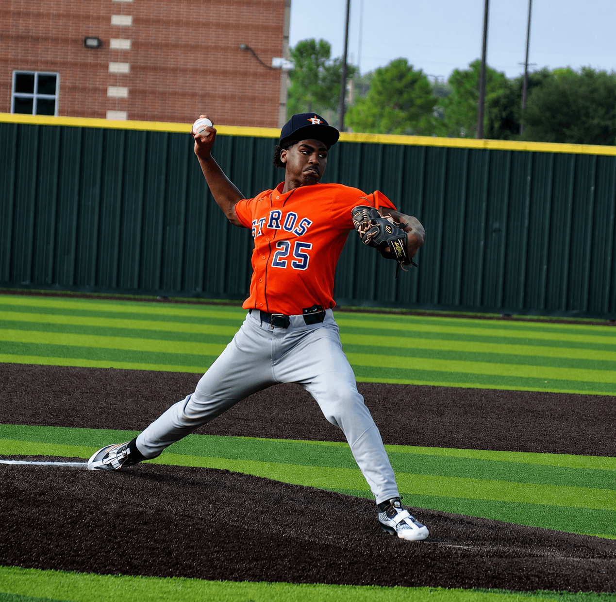 Baseball pitcher in orange jersey and gray pants throws a pitch on the mound outdoors.