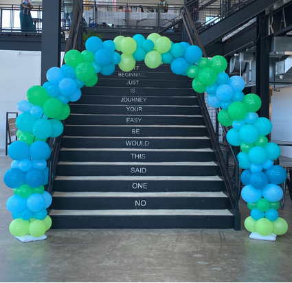 Staircase decorated with blue, green, and yellow balloons, with motivational words on each step, in a modern building.