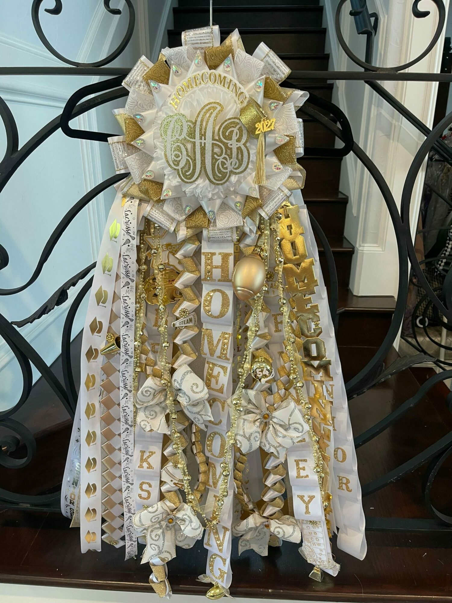 Decorative gold and white birthday cake with candles, ribbons, and a gold spoon on a table.