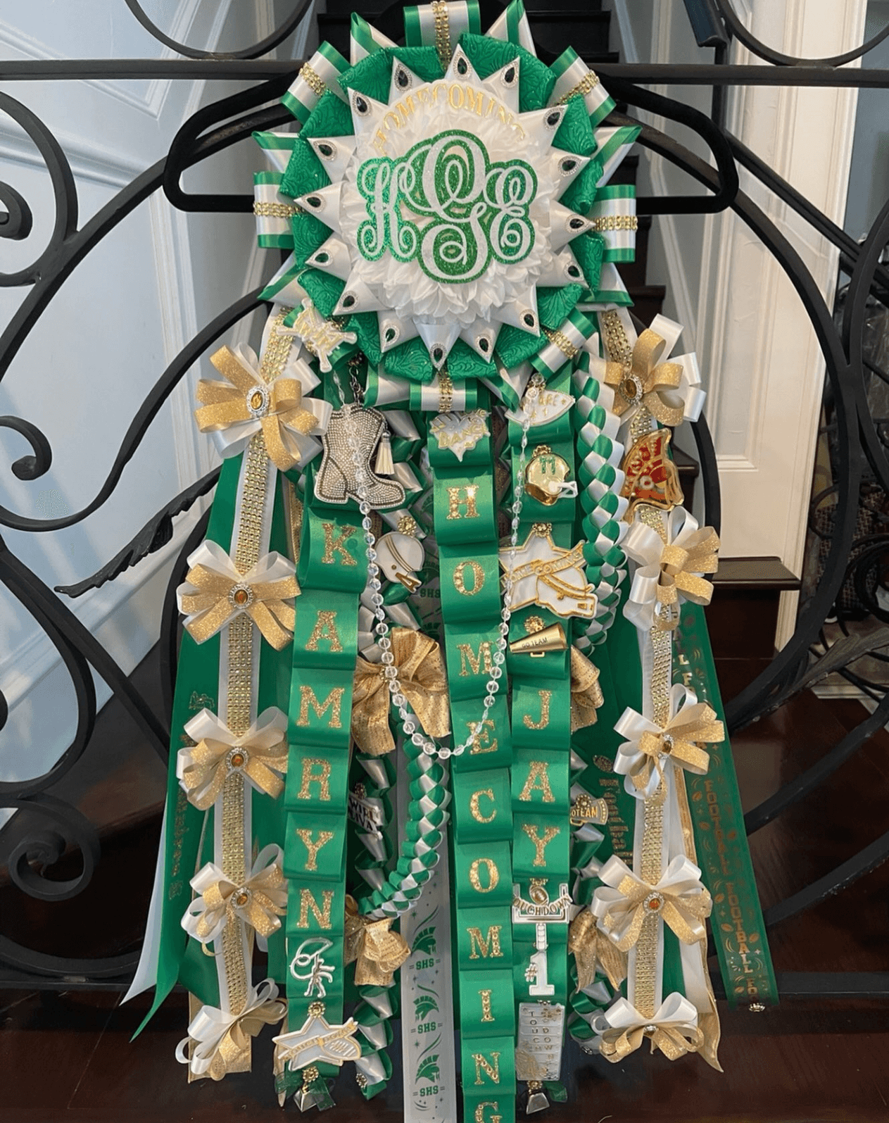 Decorative green and white ribbon arrangement with bows, beads, and a central monogram, likely for a celebration or event.
