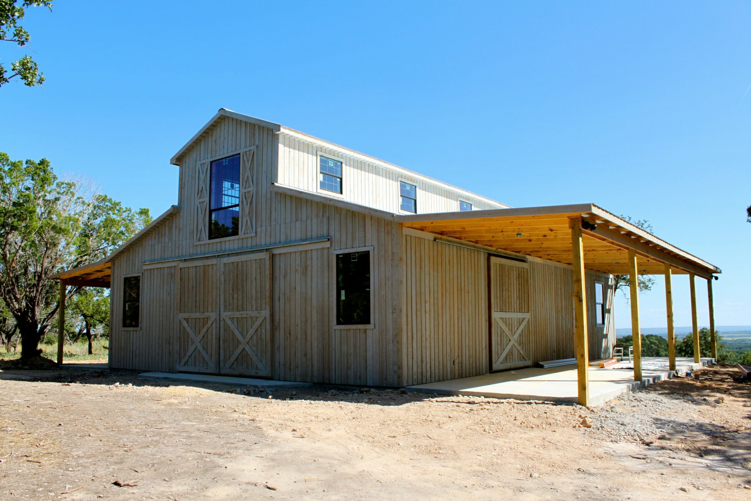 Wooden barn with a second-story addition, large sliding doors, and a covered porch area, set against a clear blue sky.