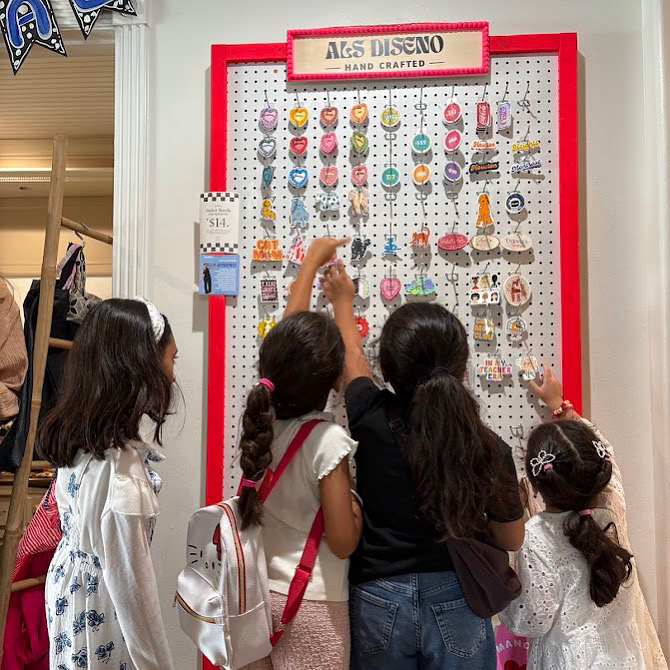Four children look at a display of colorful handmade jewelry and accessories on a pegboard at a craft store.