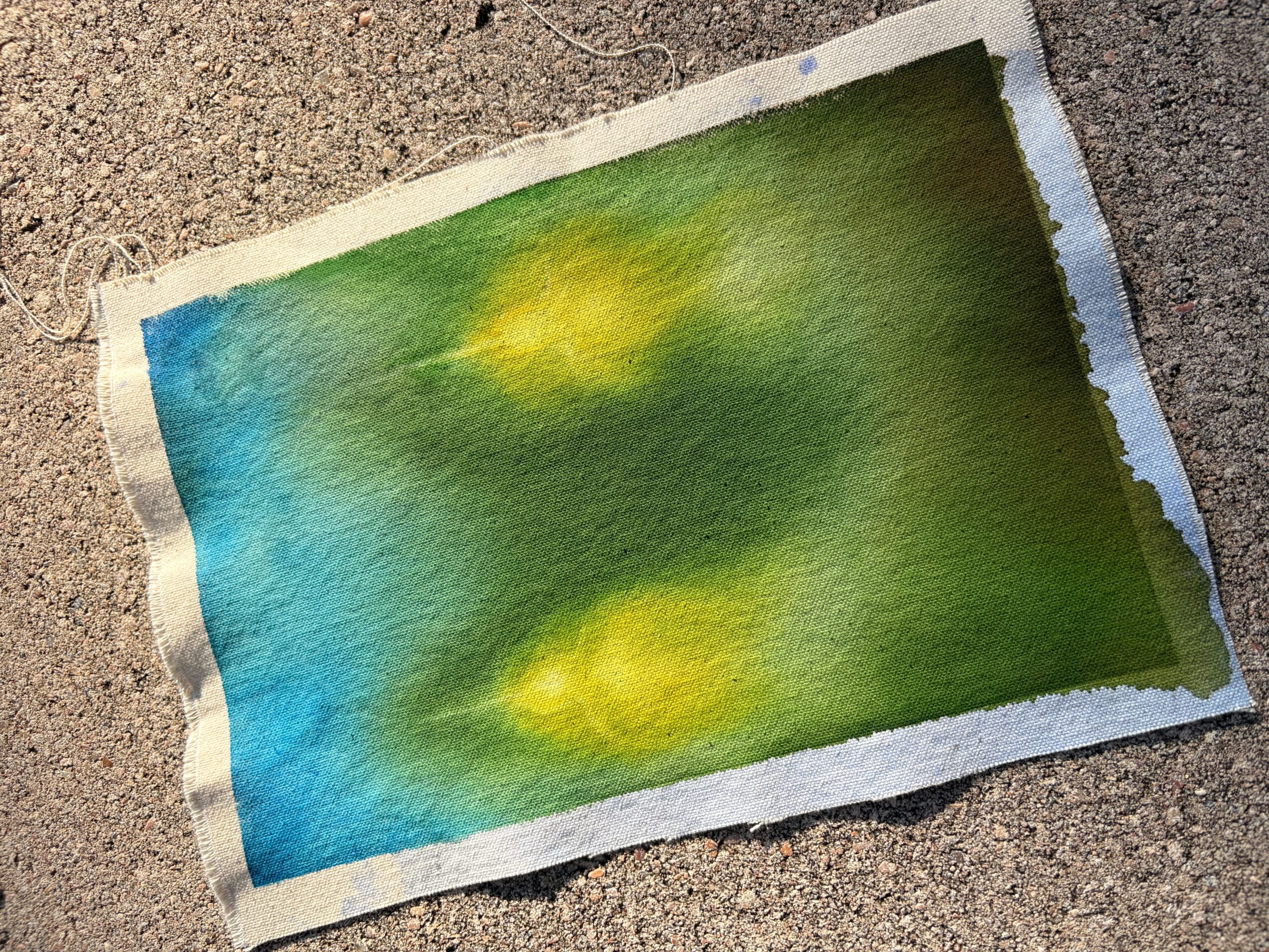 Colorful watercolor paper with blue, green, and yellow hues, placed on a rough surface.