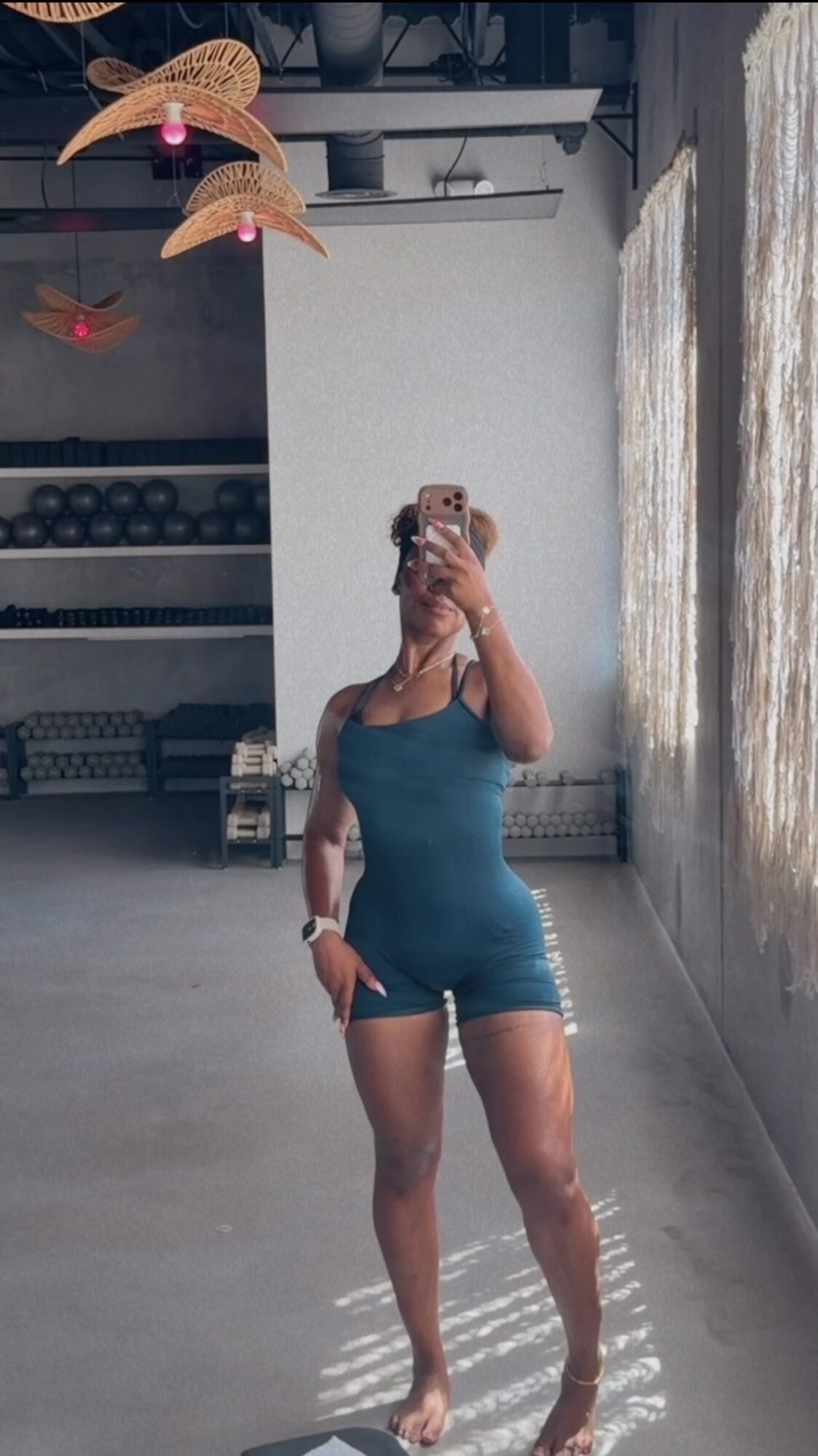 Person taking mirror selfie in a gym, wearing a blue workout outfit, with gym equipment in background.