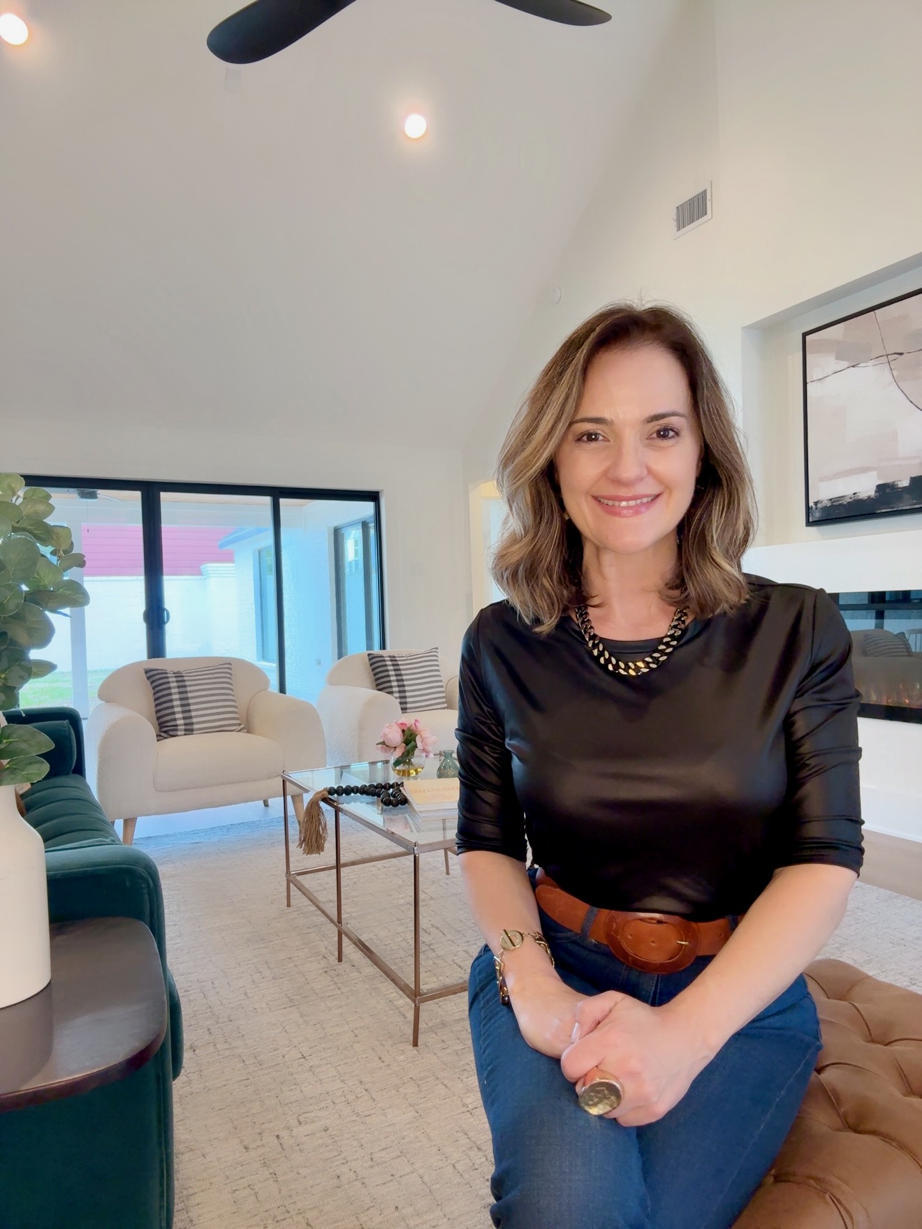 Smiling woman with shoulder-length hair wearing a black top and jeans in a modern living room.