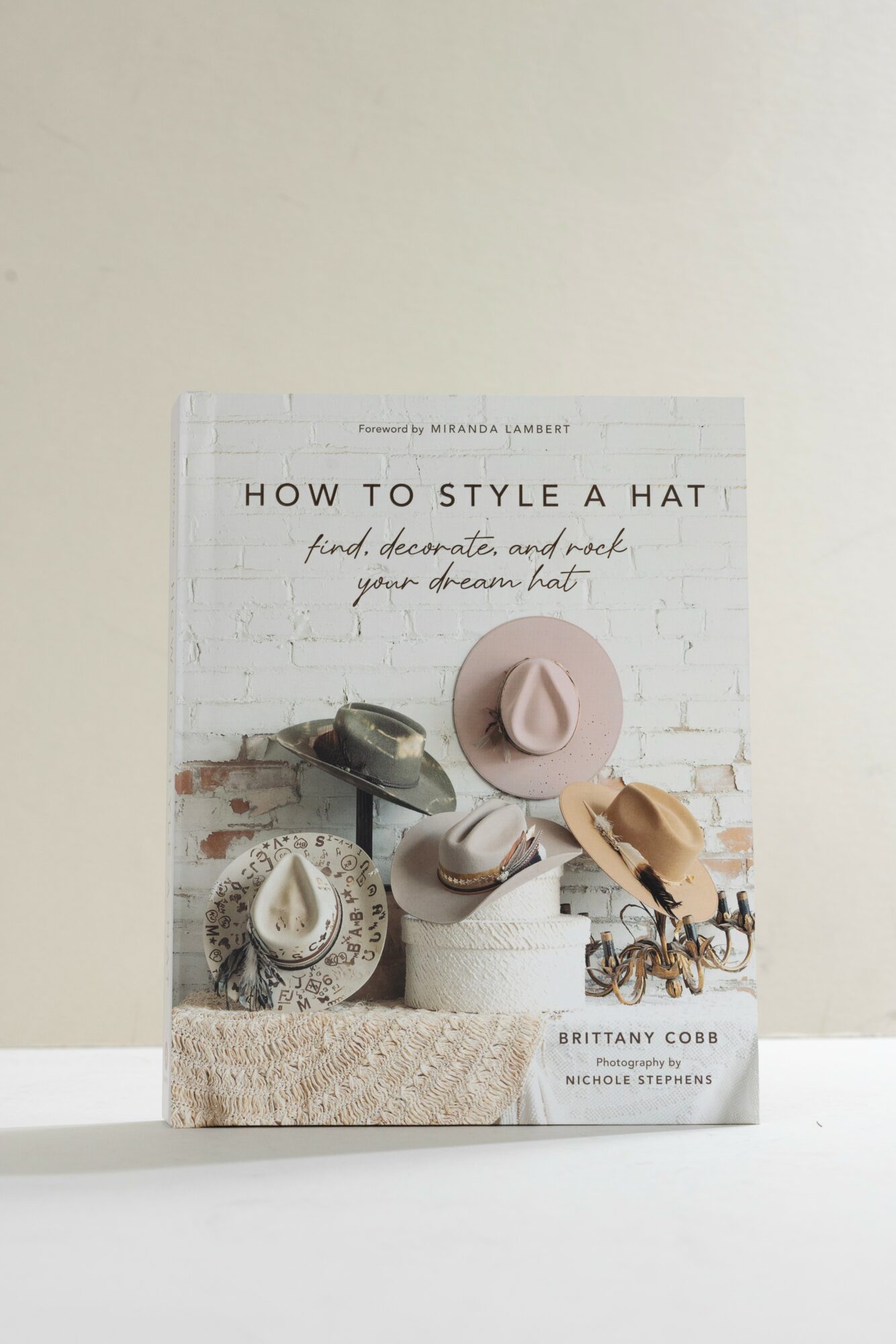 Book cover titled 'How to Style a Hat' with images of various hats and accessories against a white brick background.