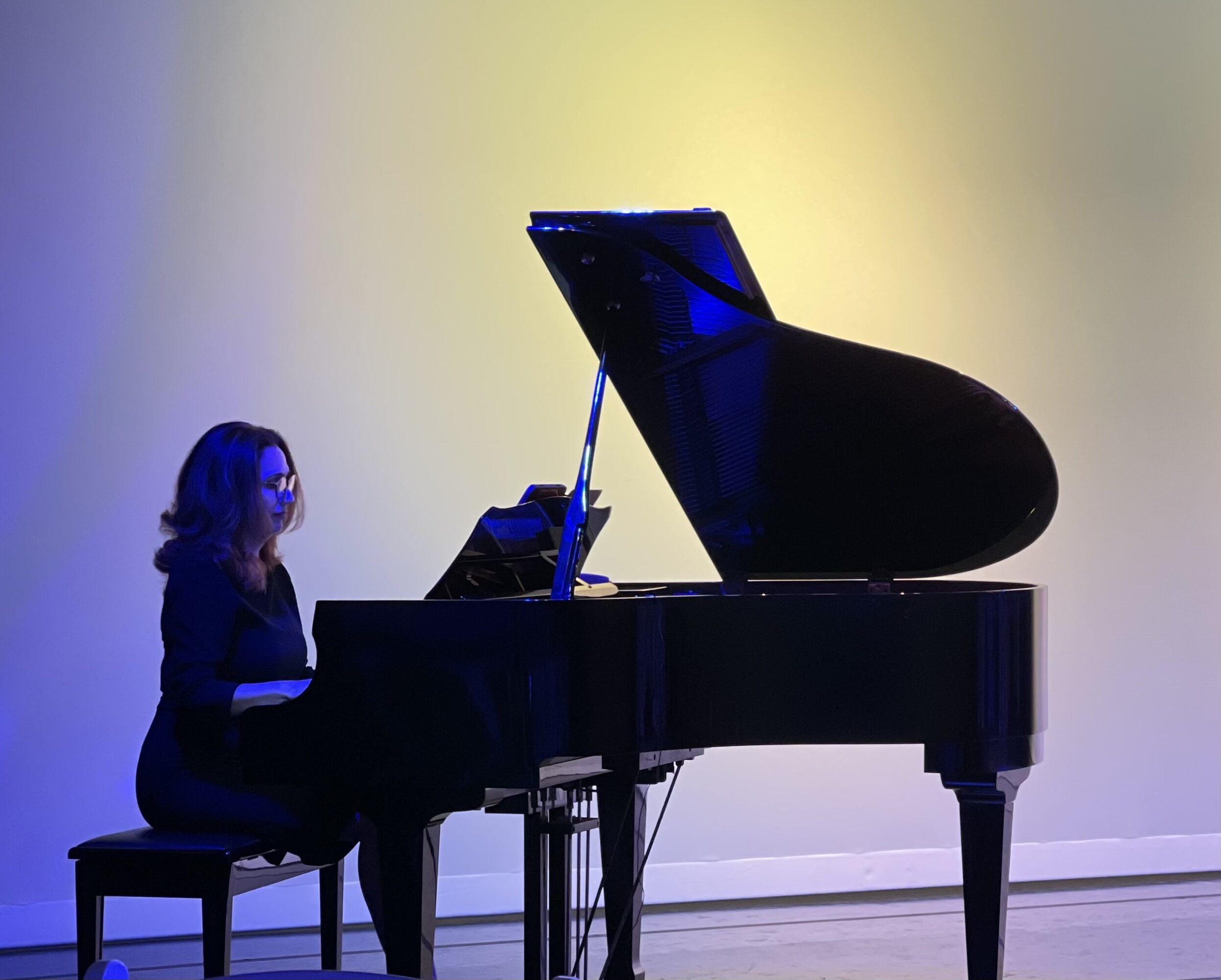 Person playing grand piano on stage with colorful background lighting
