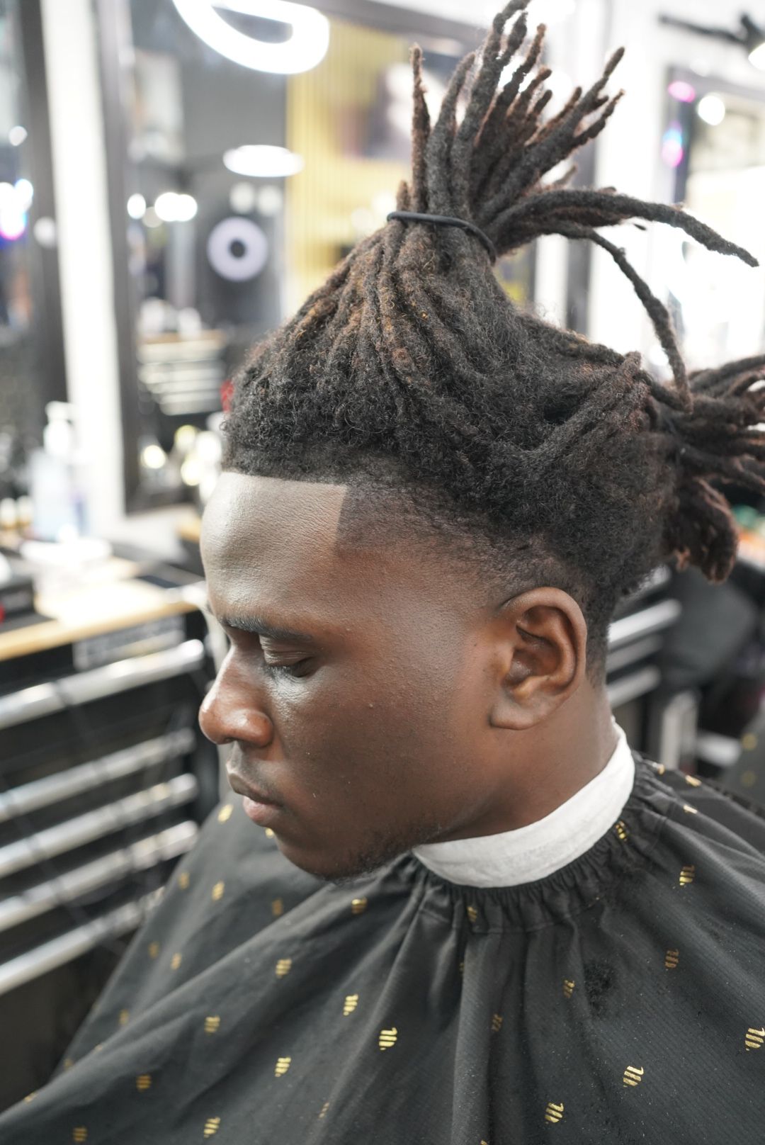 Person with styled dreadlocks lying down, head tilted back, in a salon or barbershop setting.