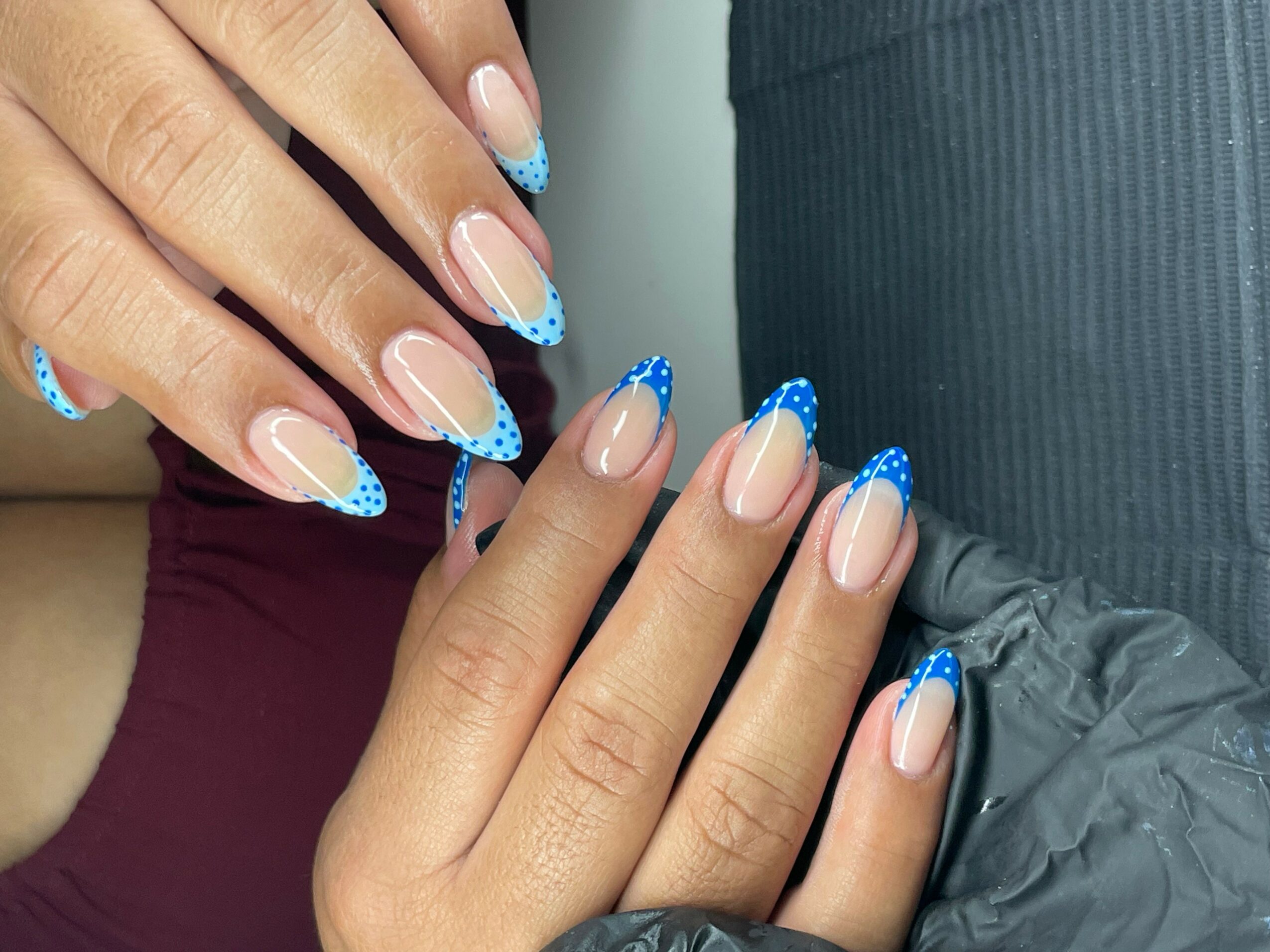 Close-up of hands with manicured nails featuring blue and white designs, resting on a dark fabric surface.