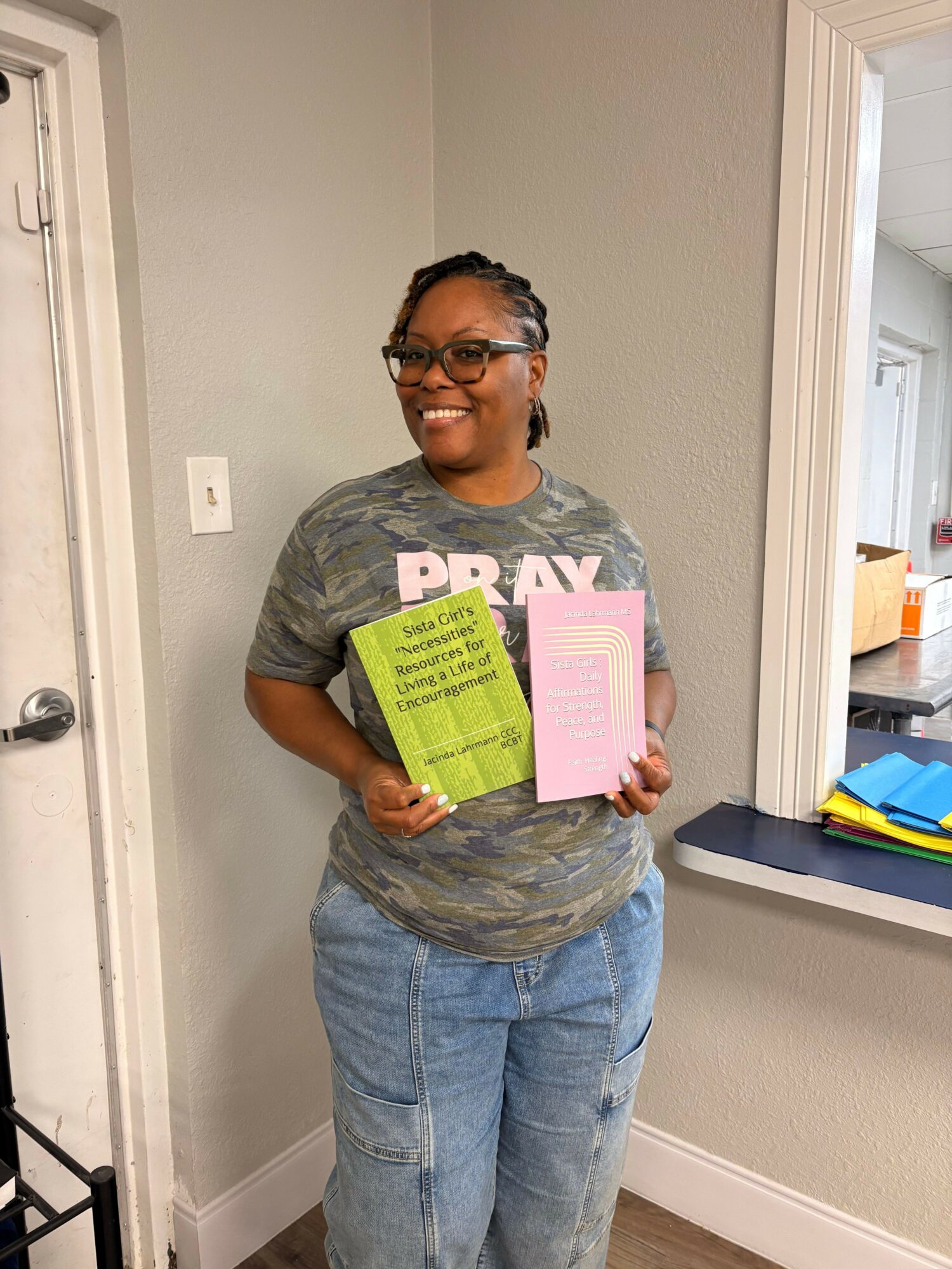 Person with glasses holding a pink and green paper, standing indoors near a door and window.