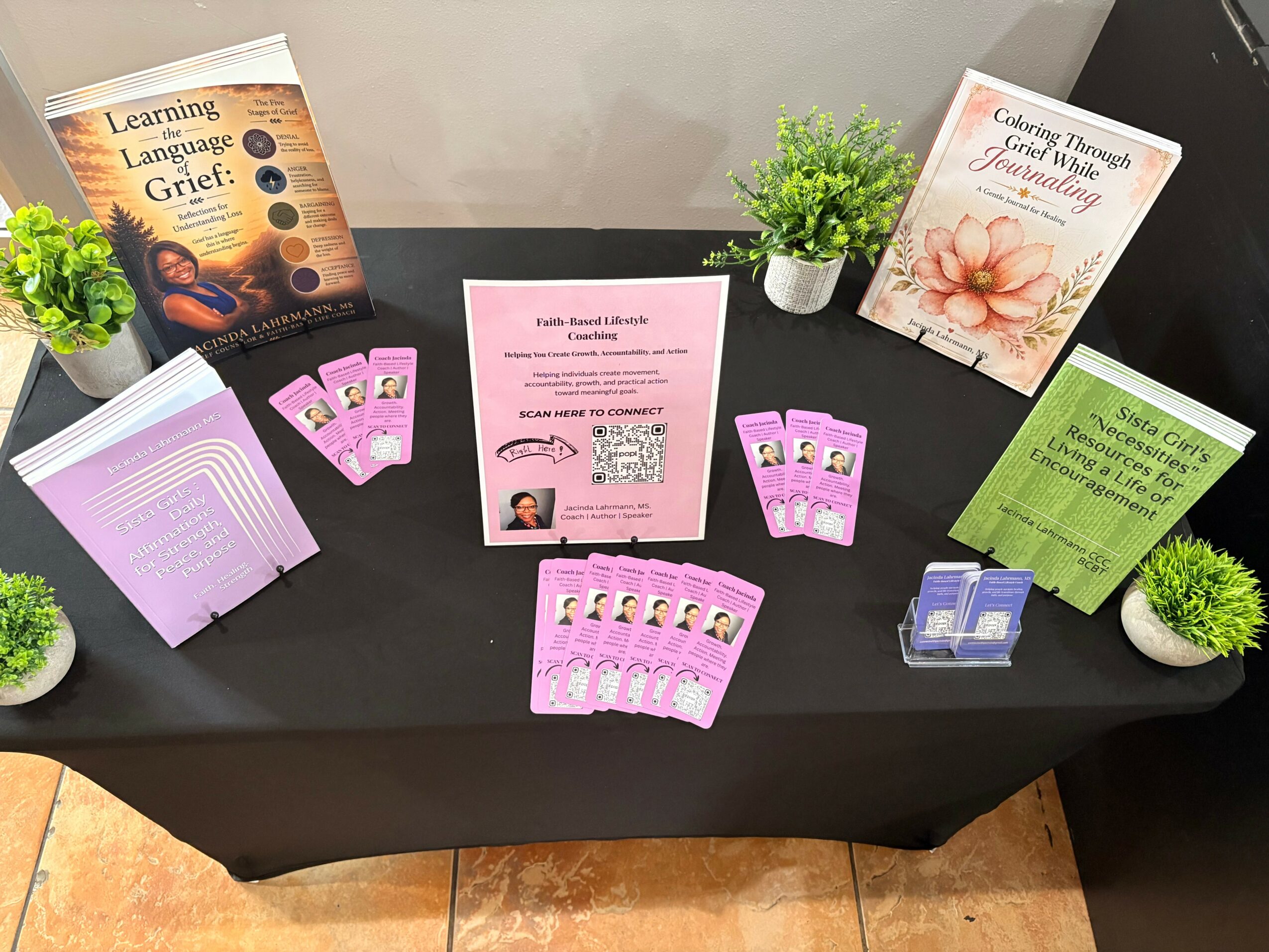 Table with books, pamphlets, and small potted plants, including a pink flyer, purple cards, and green informational sheets.