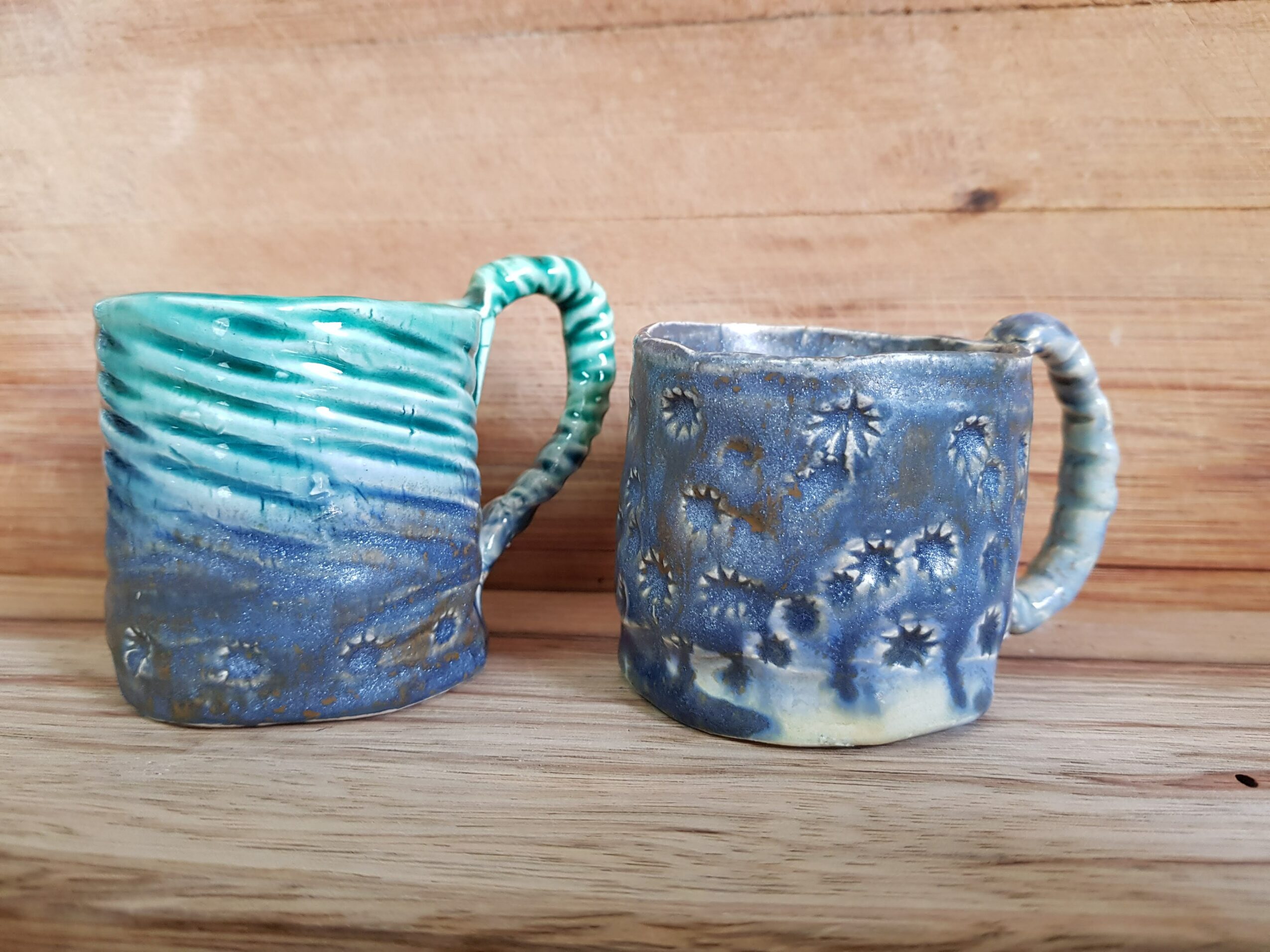 Two ceramic mugs with textured surfaces and handles, placed on a wooden surface against a wooden background.