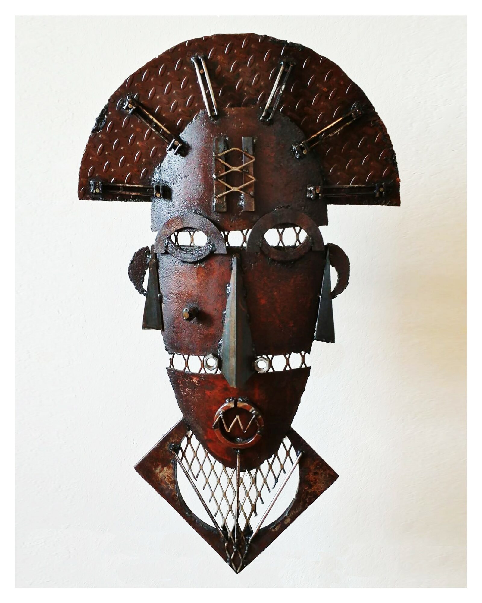 Metal African mask with geometric patterns, circular eyes, and a semi-circular headdress, mounted on a white background.