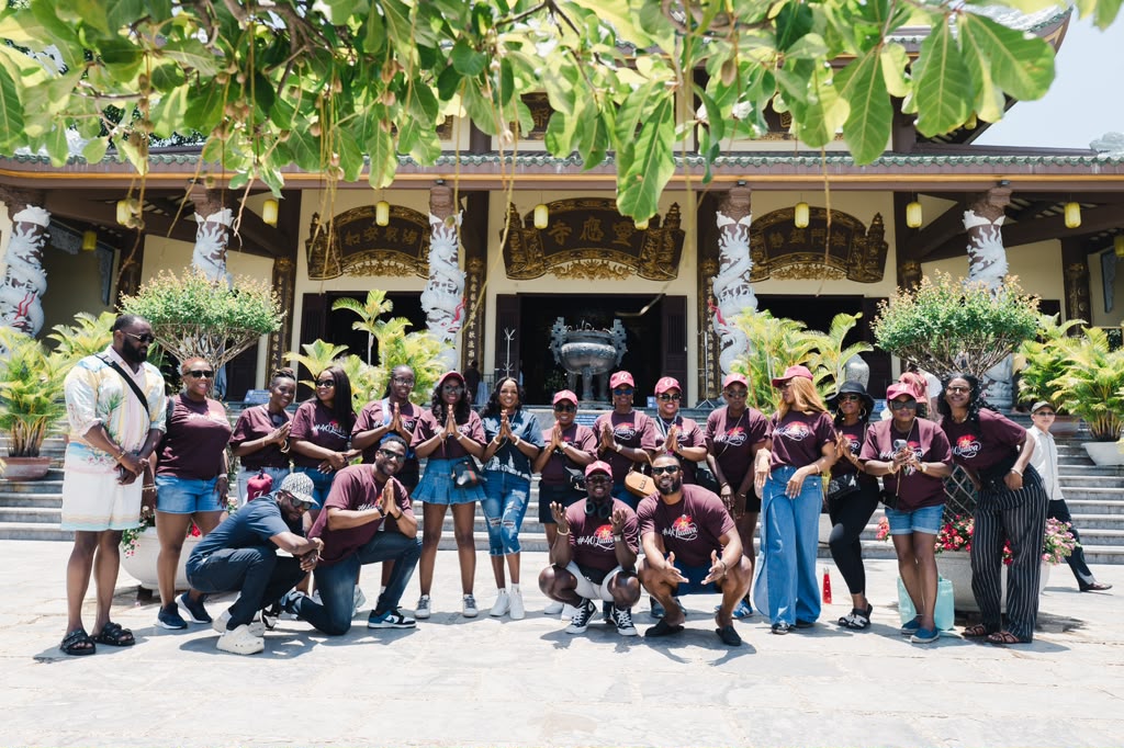 Group of people posing in front of a temple with ornate architecture and greenery, some making peace signs.