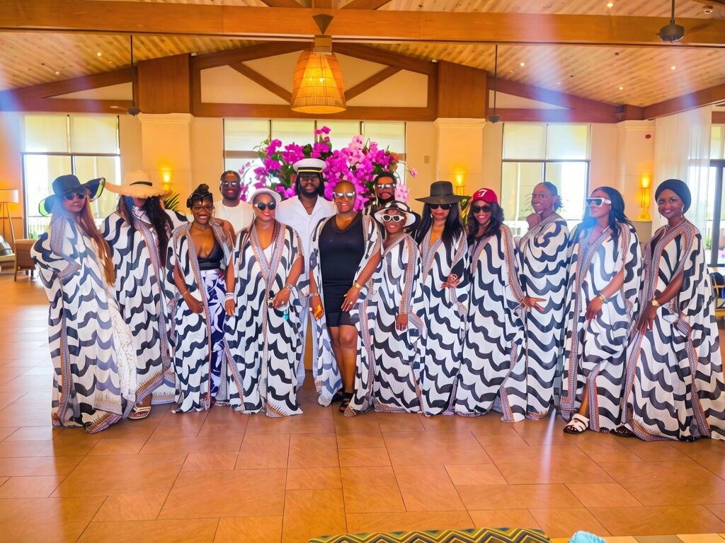 Group of women in matching striped dresses and hats, standing indoors with a floral arrangement behind them.