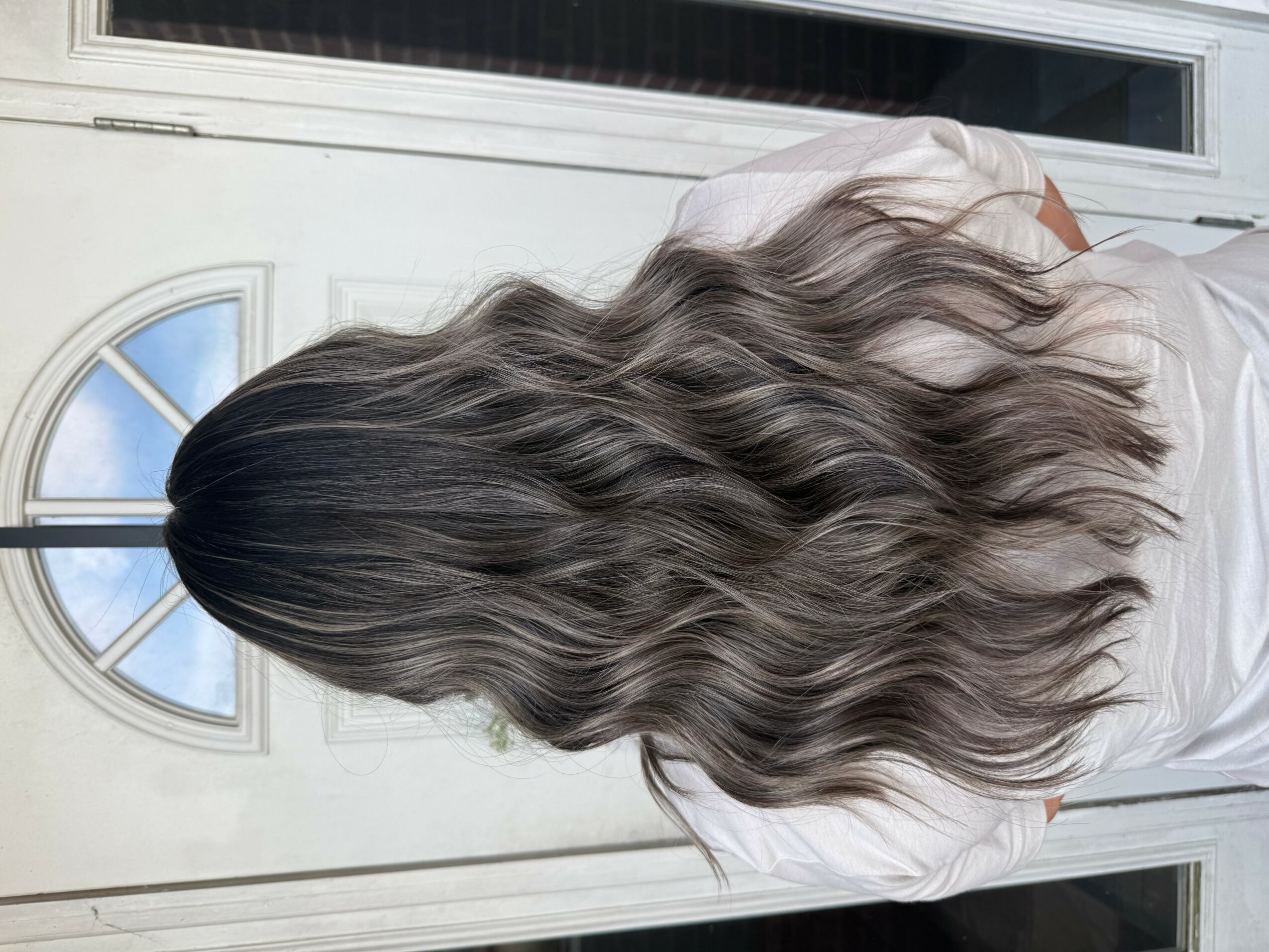 Person with long, wavy hair standing outside a door with a window, facing away from the camera.