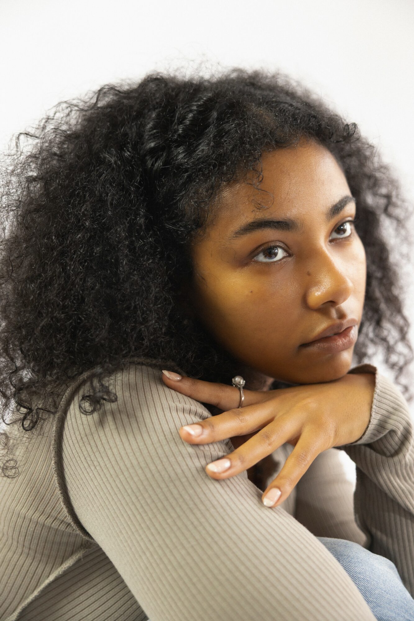 Young woman with curly hair resting her chin on her hand, looking at the camera.