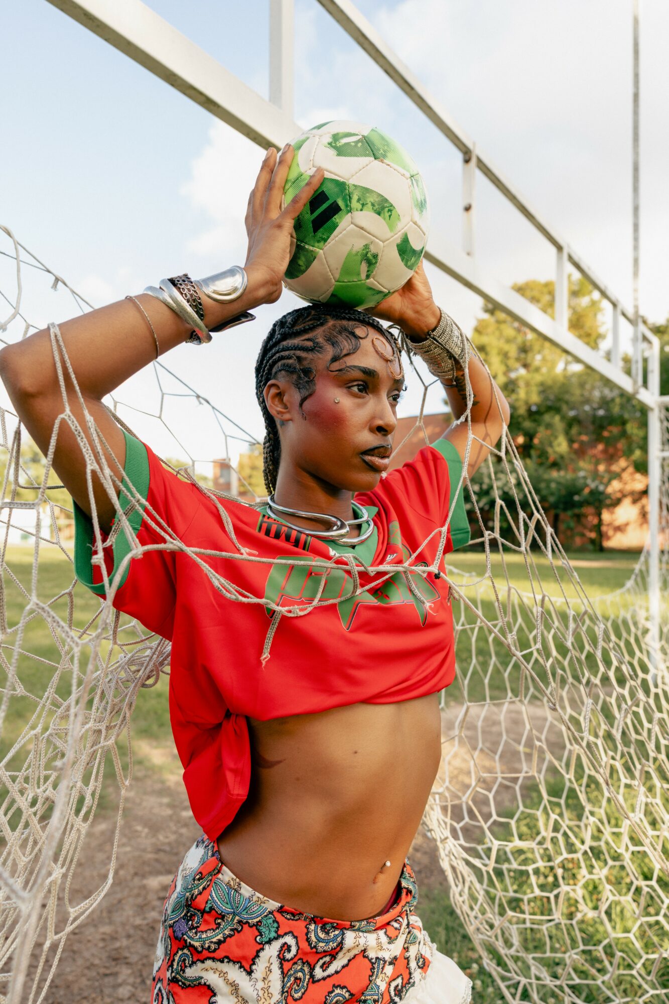 Young woman holding a soccer ball above her head, standing in front of a goal net outdoors.
