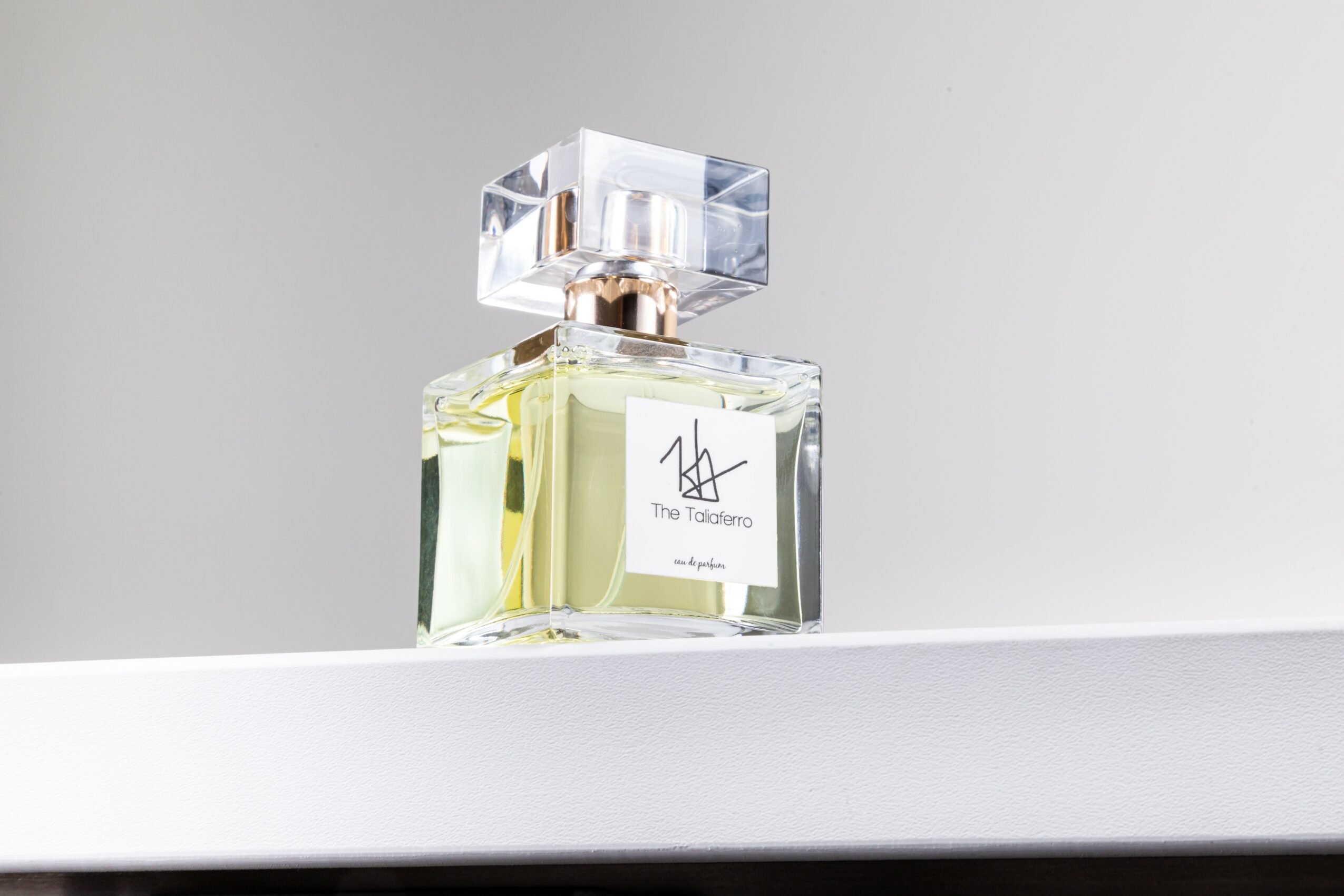A perfume bottle with a clear rectangular glass body, a white label, and a large, transparent, square cap, placed on a white surface.