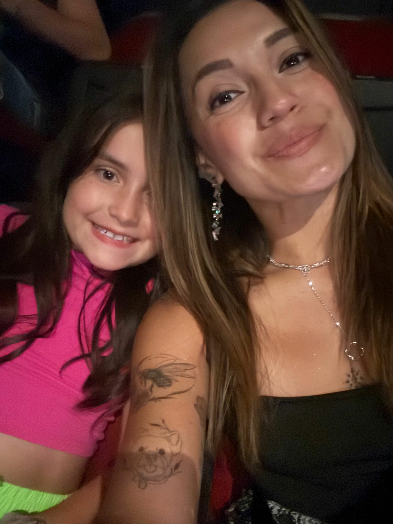 Two women smiling, one with long hair and tattoos, the other with long dark hair, wearing a pink top.