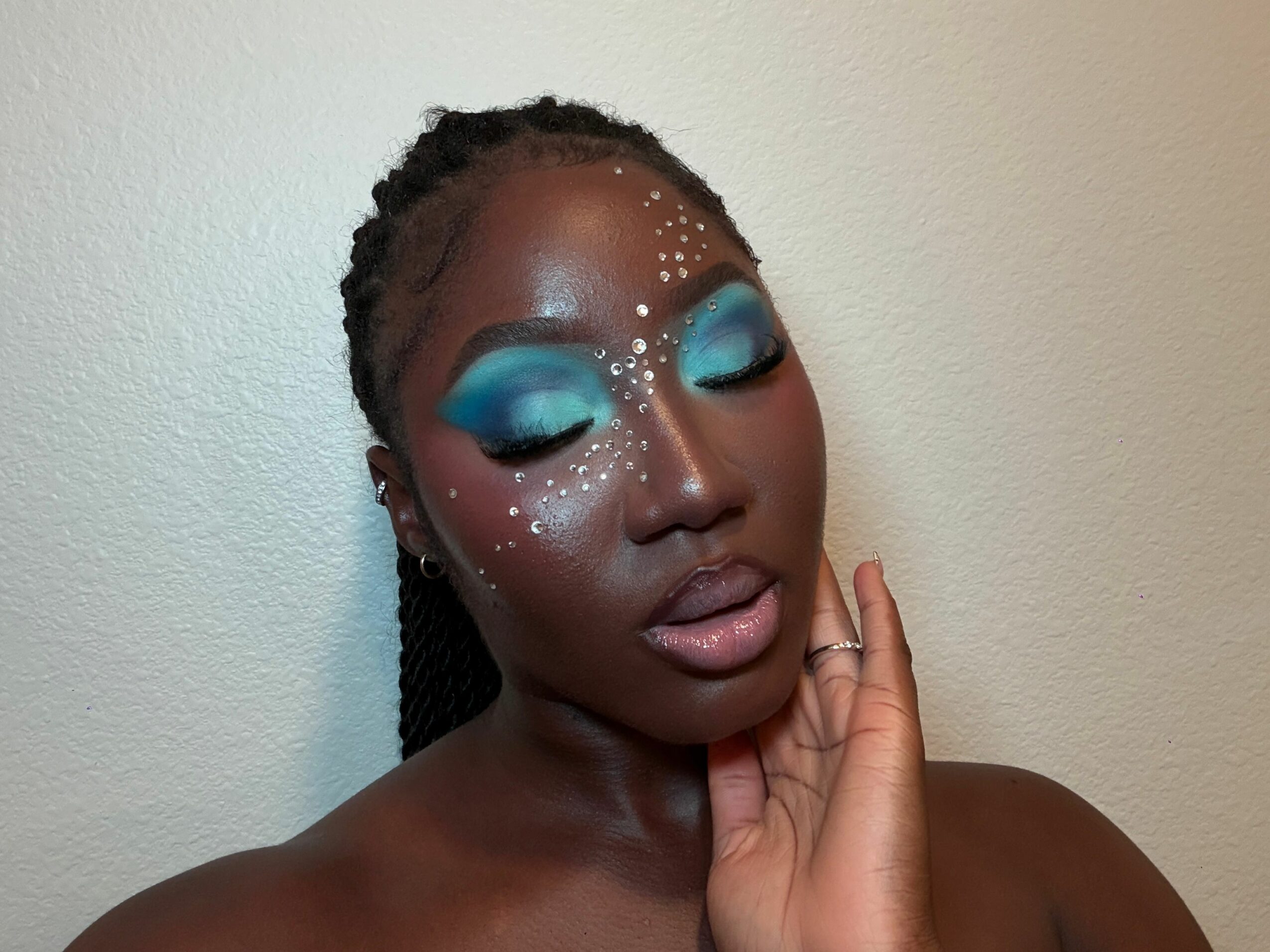Person with blue eye makeup, glitter, and closed eyes, holding hand near face, upside down.