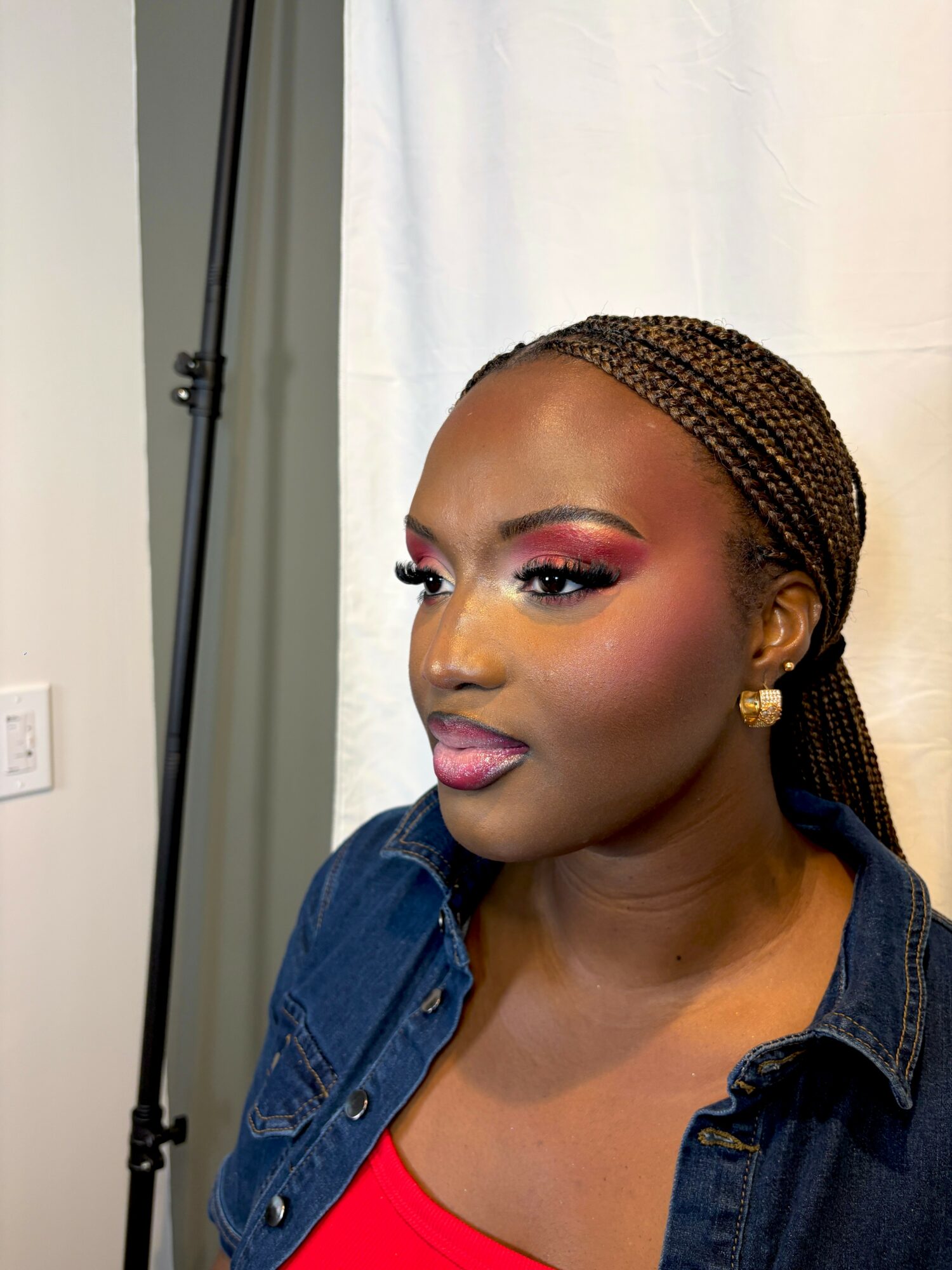 Portrait of a woman with braided hair, wearing makeup, a denim jacket, and a red top, against a white background.