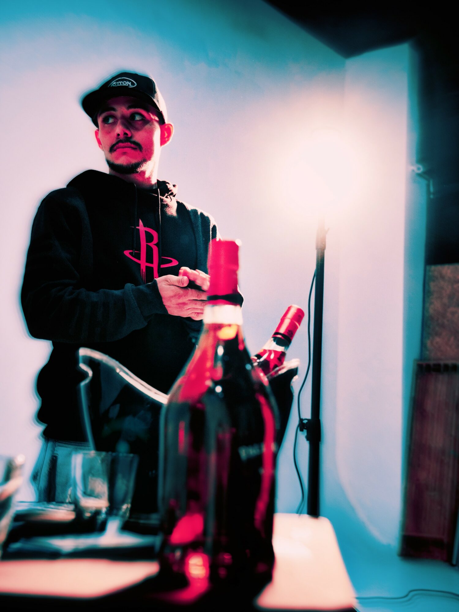 Person holding a red candle, standing behind a table with bottles, in a room with blue and white lighting.