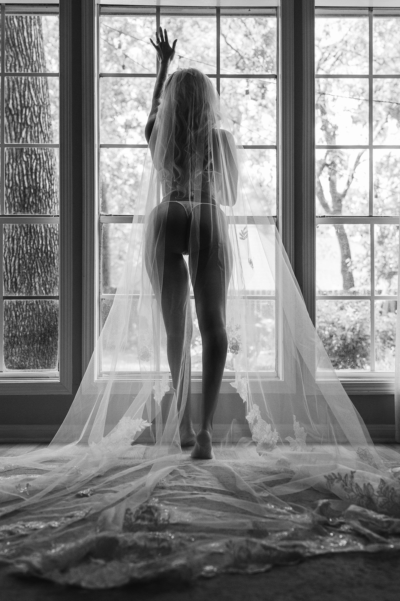 Silhouette of a woman standing by a window, with sheer curtains flowing to the floor, backlit by outdoor light.