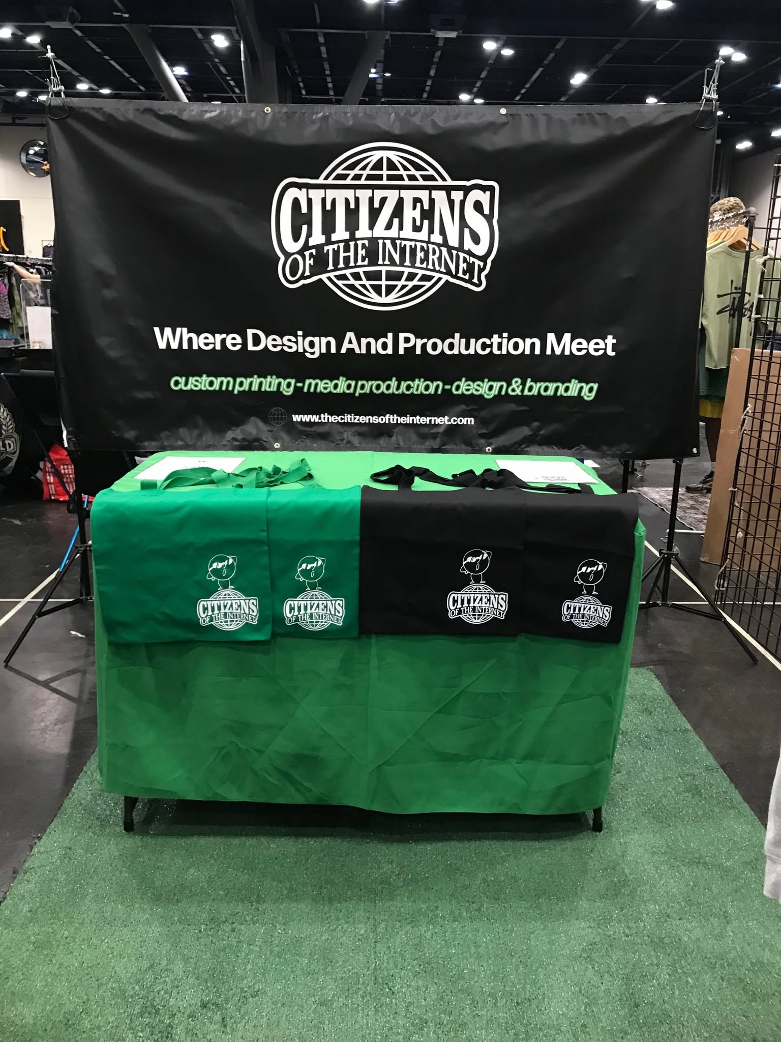 Display booth with a black banner reading 'Citizens of the Internet' and a green tablecloth with three logos, set on green carpet.