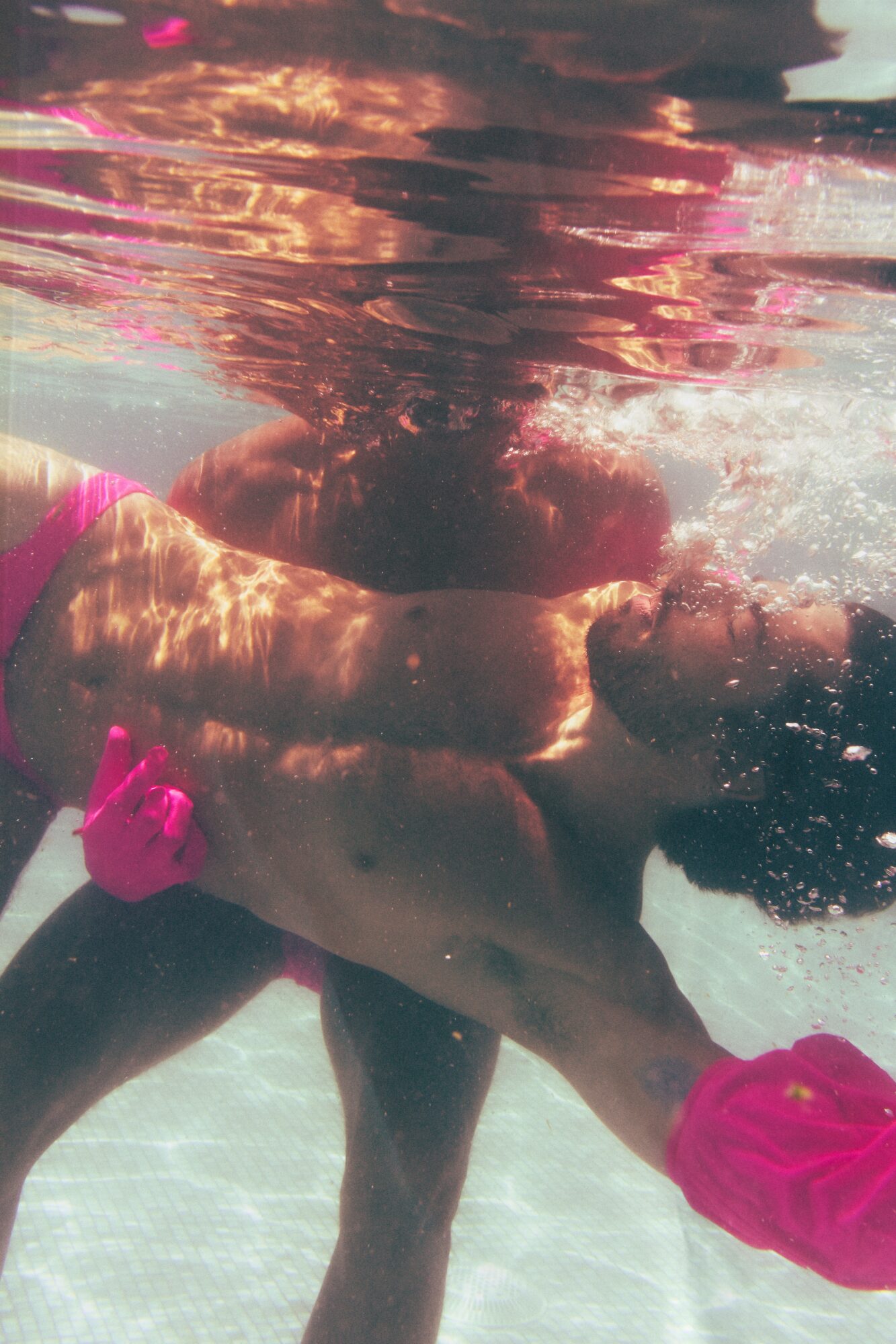 Person floating in water with pink accessories, partially submerged, with sunlight reflections on the surface.