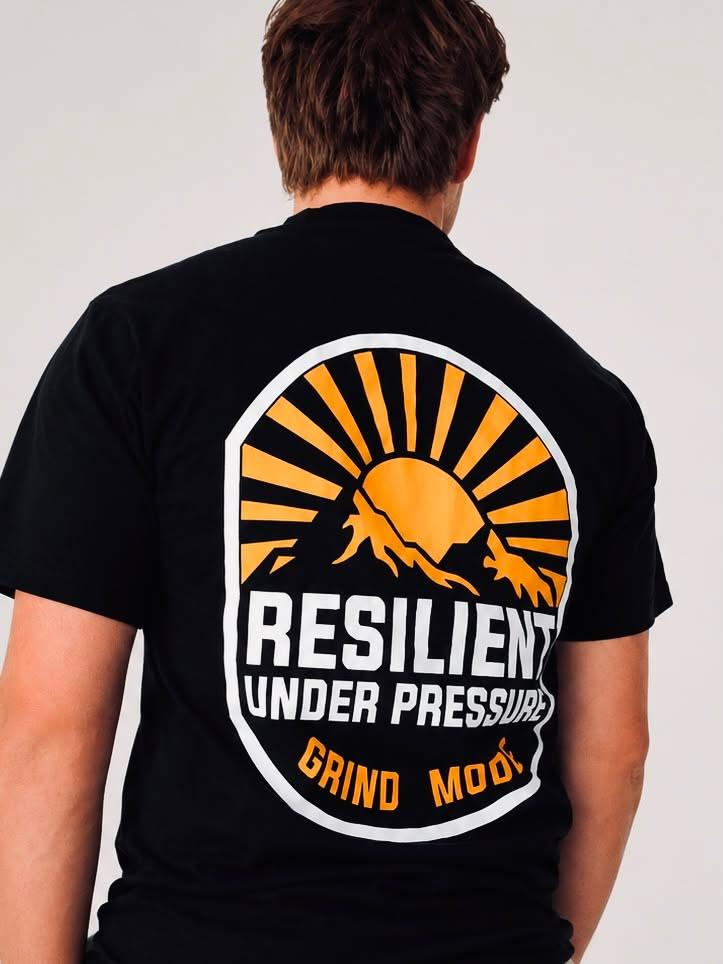 Back view of a person wearing a black T-shirt with a circular graphic design featuring a mountain and sun, and text.