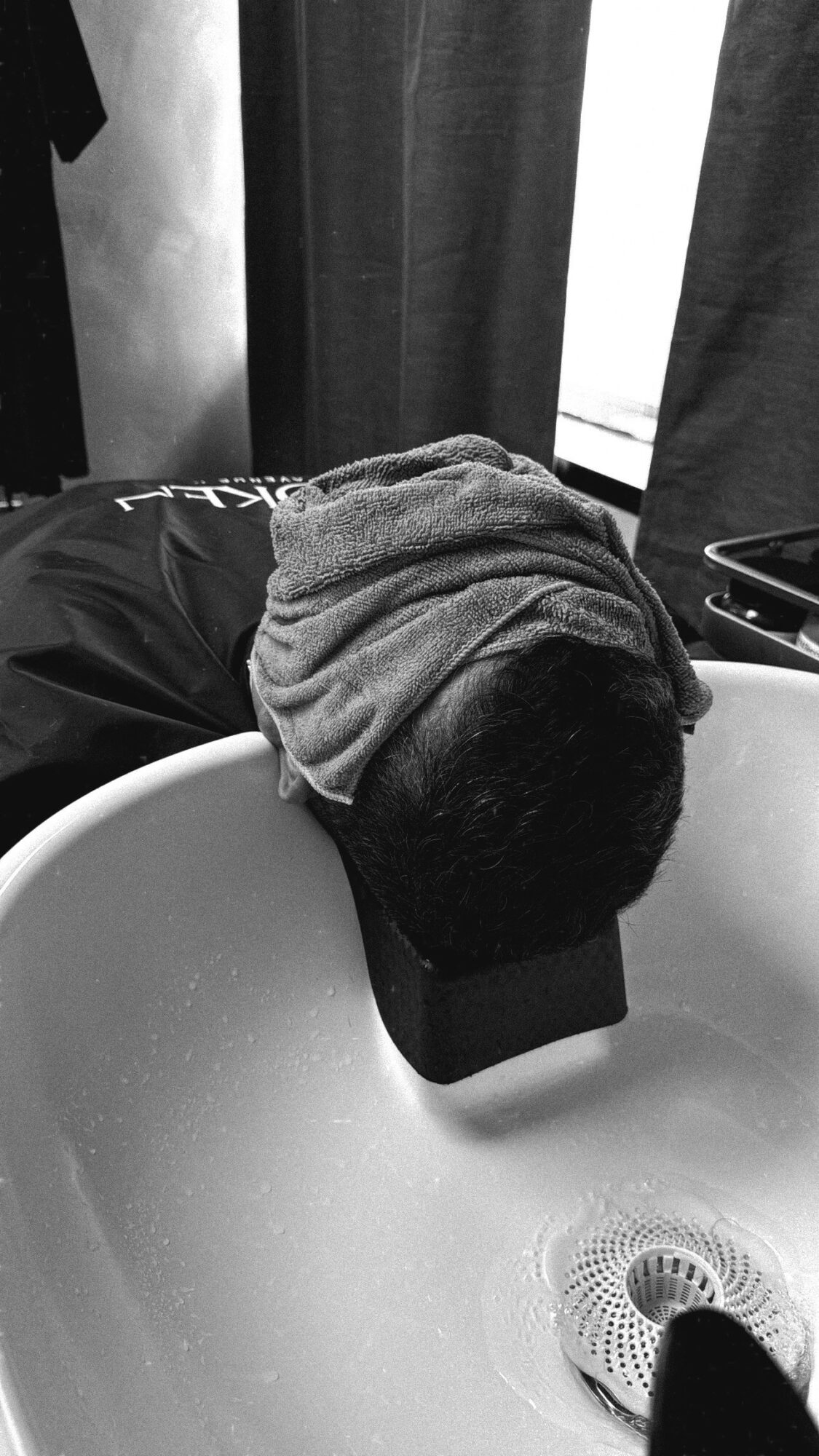 Gray hoodie draped over a black cap resting on a white sink, with dark curtains in the background.