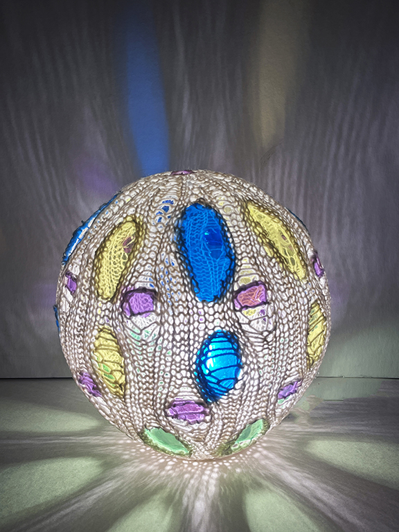 Decorative spherical object with colorful oval and circular patterns, illuminated from below, with a blurred background.