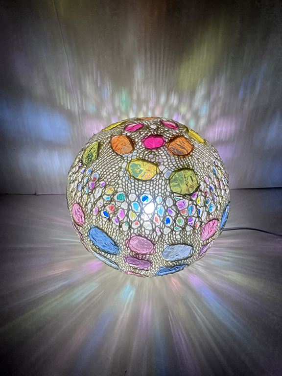 Colorful spherical lamp with multicolored patches, projecting light and patterns onto surrounding surfaces.