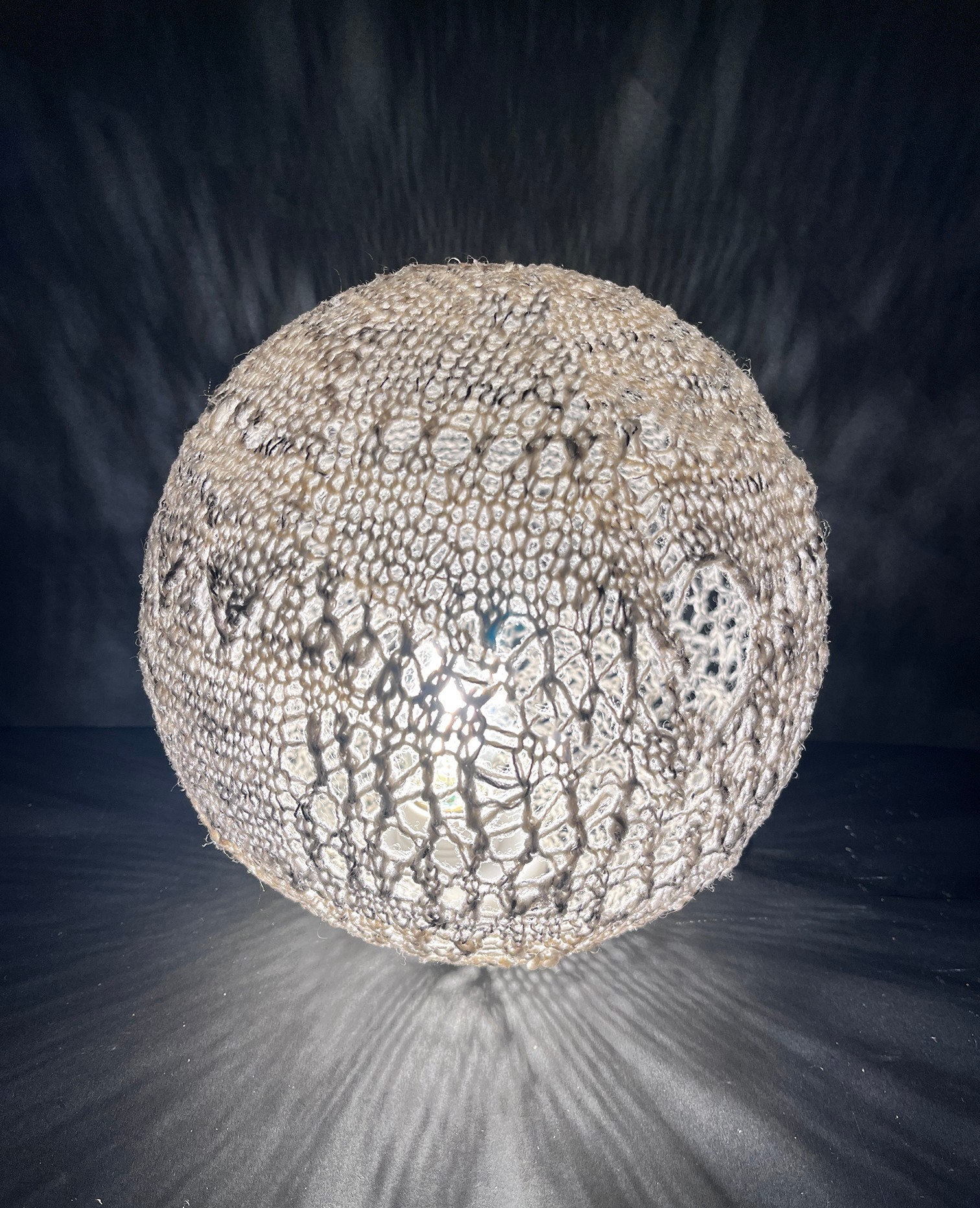 A spherical object with a textured, patterned surface resembling a seed or fruit, against a dark background with light rays.